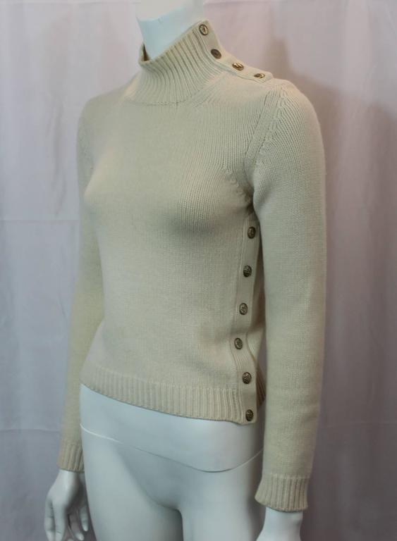 Chanel Ivory Cashmere Knitted Turtleneck with Gold Button Details -36 - 04A. This beautiful turtleneck is ivory colored and has gold buttons. Snap buttons go all along the left side and the left side of the bodice. The buttons have the Chanel logo