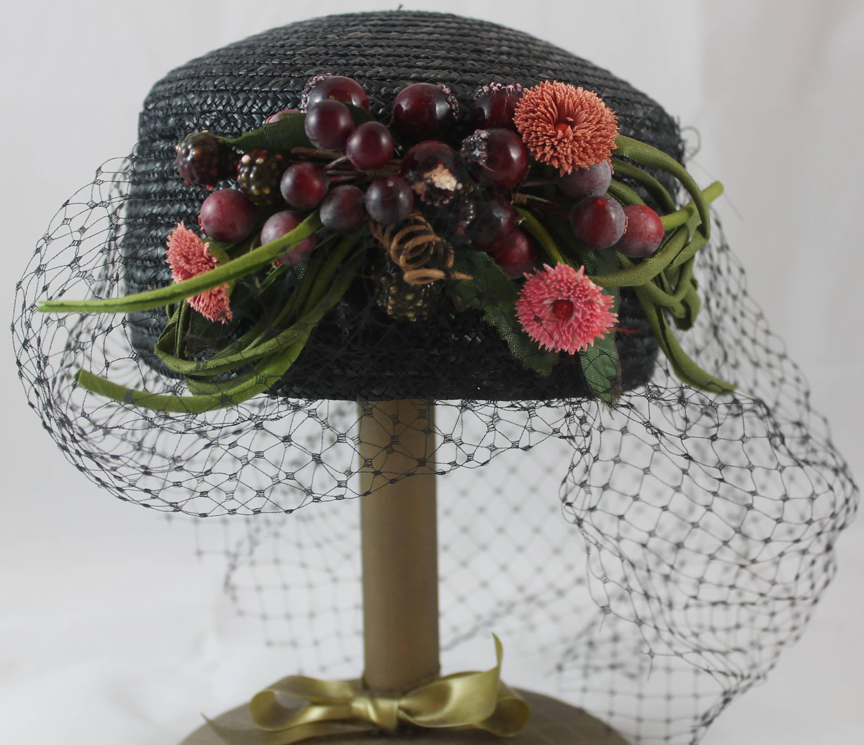 Vintage Black Straw Hat with Net and Plastic Fruit. This straw pill box hat has hanging black mesh and plastic fruit clustered in the front. It is in very good condition with a couple ares on the mesh that are ripped.

Measurements
Circumference: