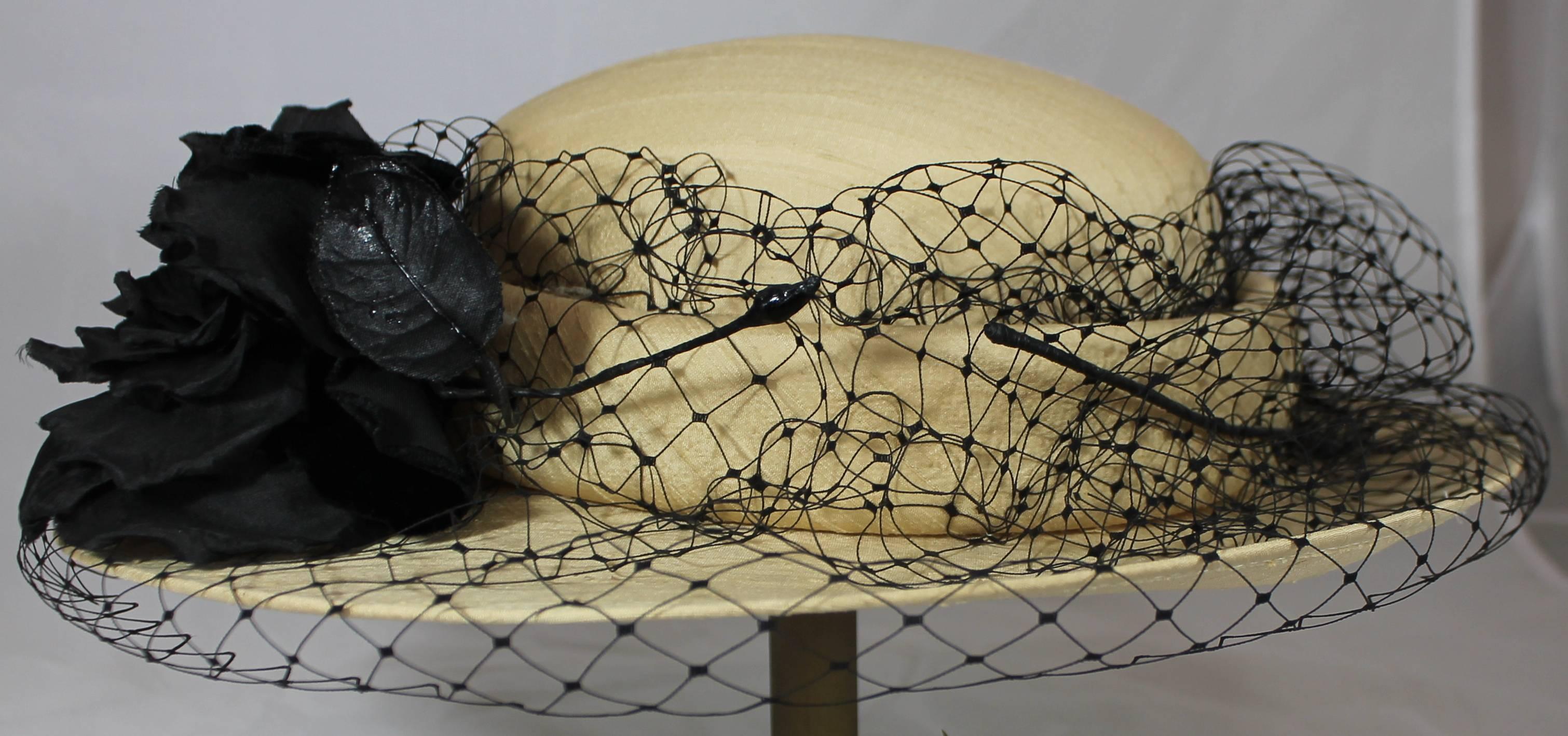 Suzanne Couture Millinery Beige Raw Silk Hat with Black Netting and Flower. This hat is a smooth beige silk and has black netting going around on top of the brim w/ leaves and a flower detail. It is in excellent