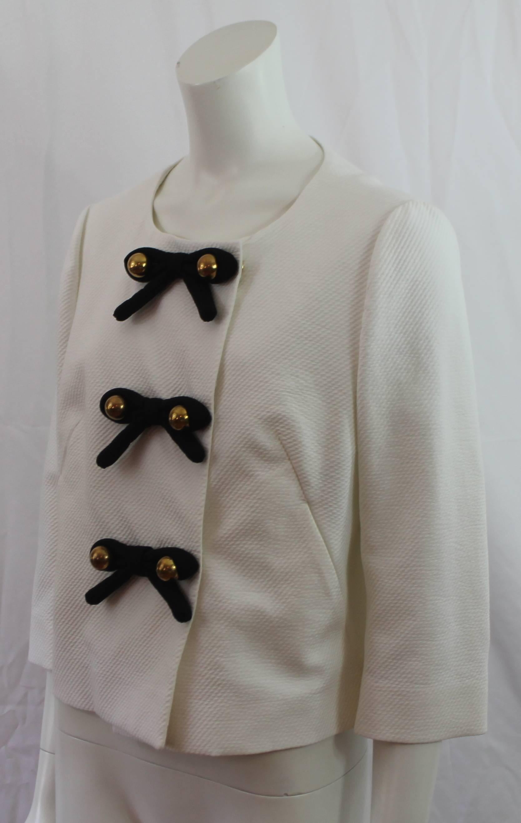Moschino C&C White Cotton Jacket with Bow Detail - M. This seersucker jacket is a classic piece and features 3 black bows with gold bead detailing, snap closures, 2 pockets, a bracelet sleeve, and a round neckline. It is in excellent condition with