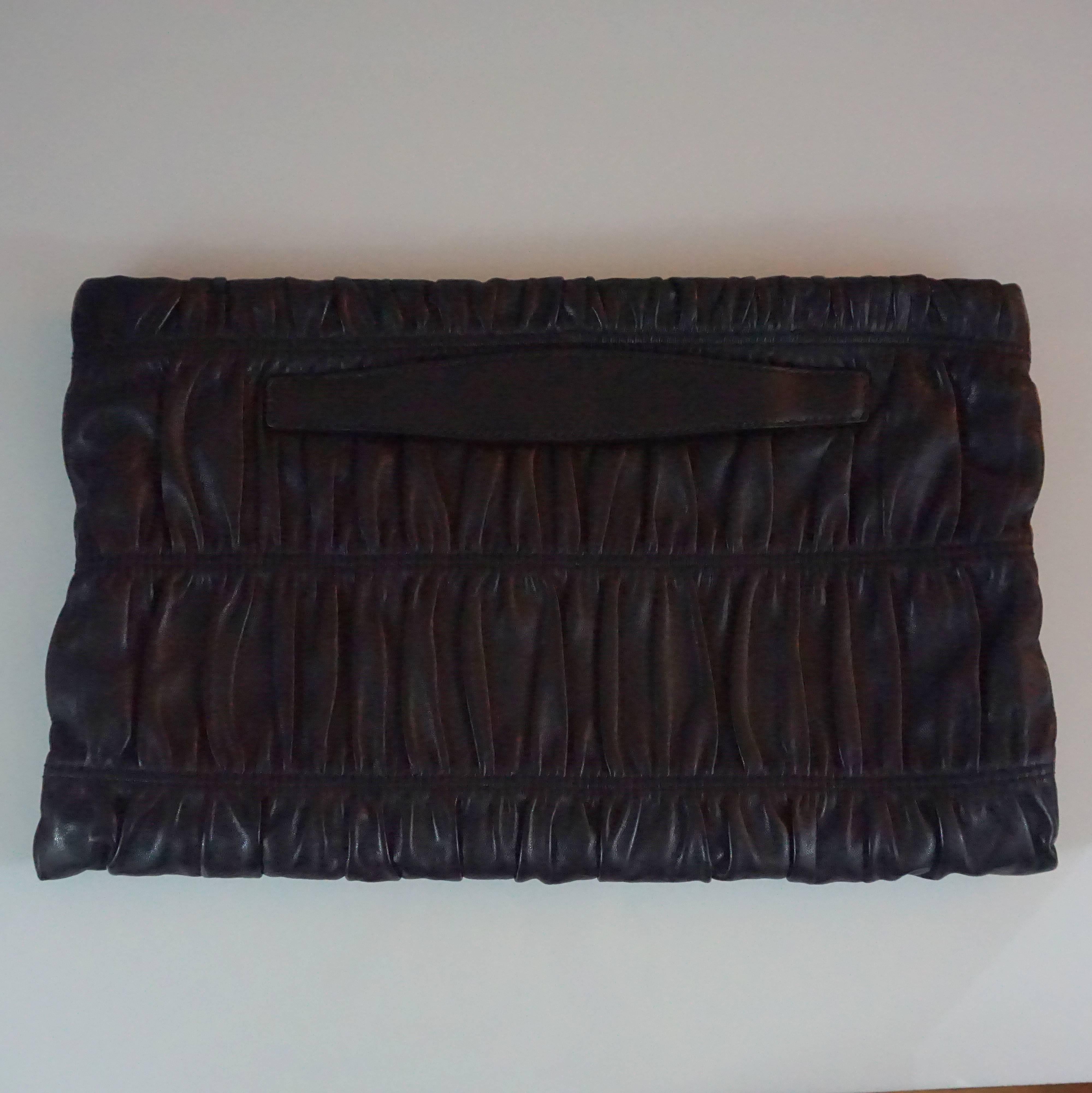 Prada Black Ruched Lambskin Nappa Gaufre Clutch - GHW. The beautiful oversized clutch is very versatile and features ruching, a gold Prada emblem, blush leather interior, 1 main compartment, 2 small side pockets, 1 one zip pocket, and a back handle.