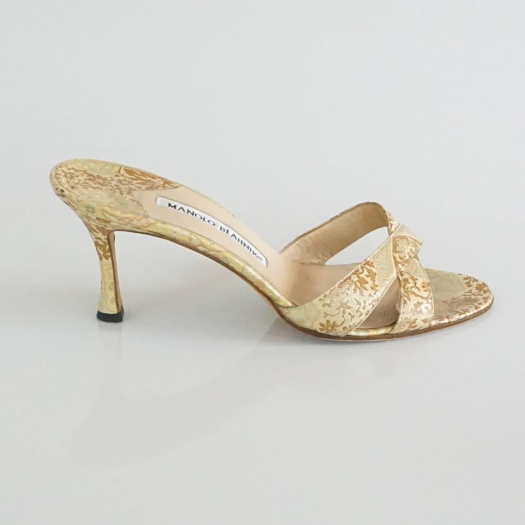 Manolo Blahnik Gold Leather Brocade Printed Slides - 37. These heels have an ornate, shimmery feel. They feature a tan and gold brocade print, crossing front straps, and a low heel. They are in excellent condition with some wear on the inside and