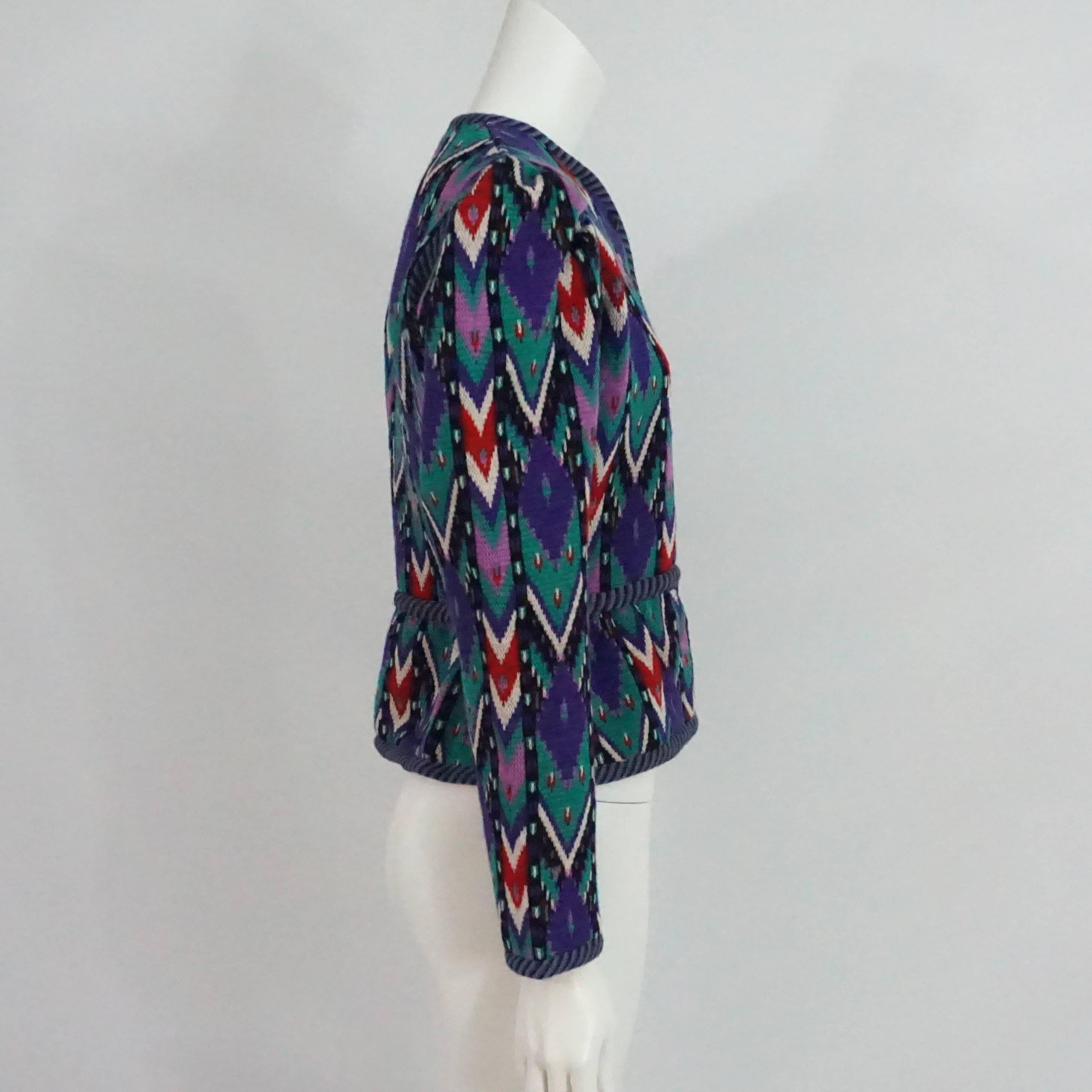 This fun and unique vintage Yves Saint Laurent sweater jacket is made of wool. It features a multi-colored chevron-like print. There is a mixture of red, black, white, green, purple, and blue. There is a slight collar, black buttons, a slight peplum