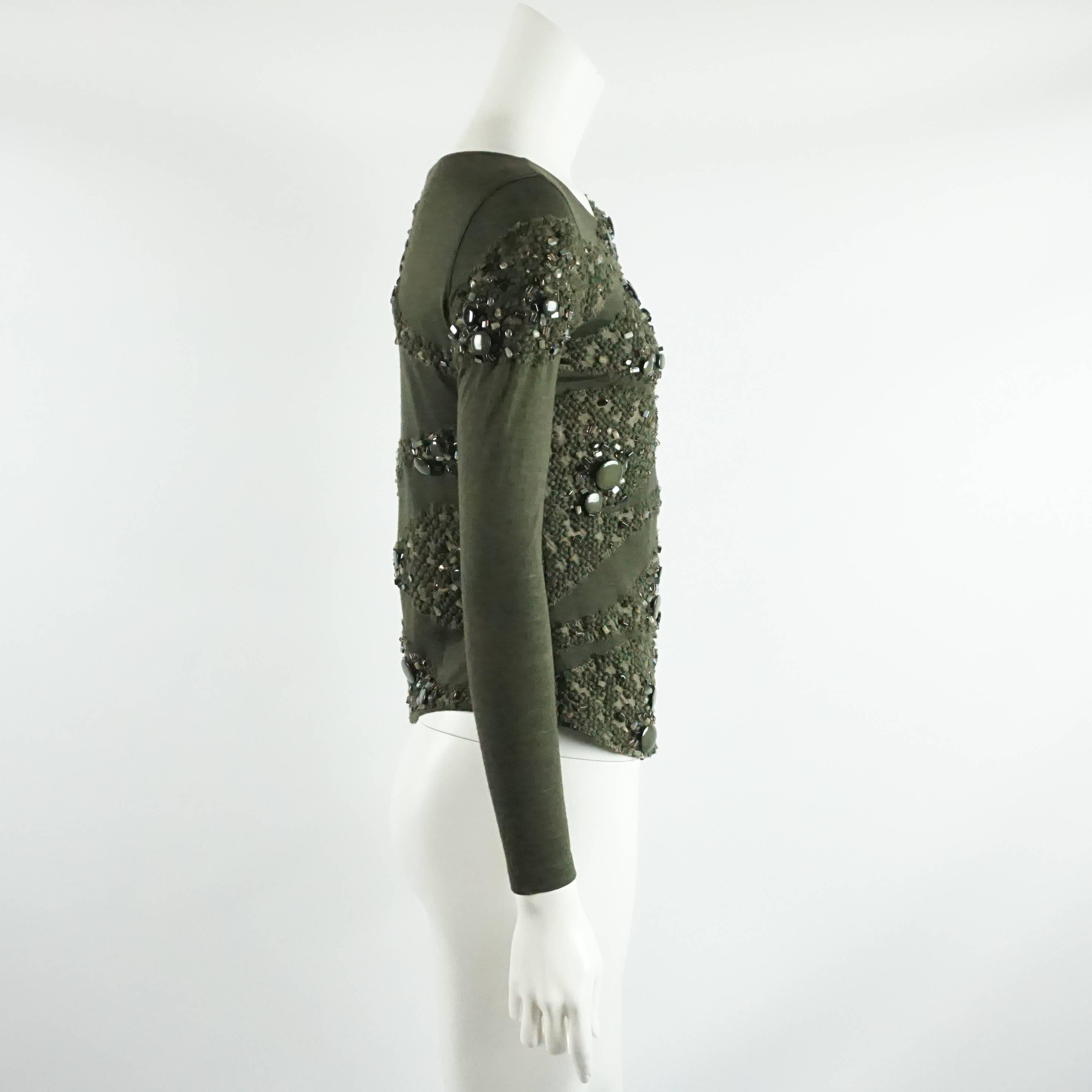 This army green long sleeved Akris top has a side zipper. It has a continuous applique with crystals, beads, and stones. This top is in excellent condition with one loose stone.

Measurements
Shoulder to Shoulder: 14