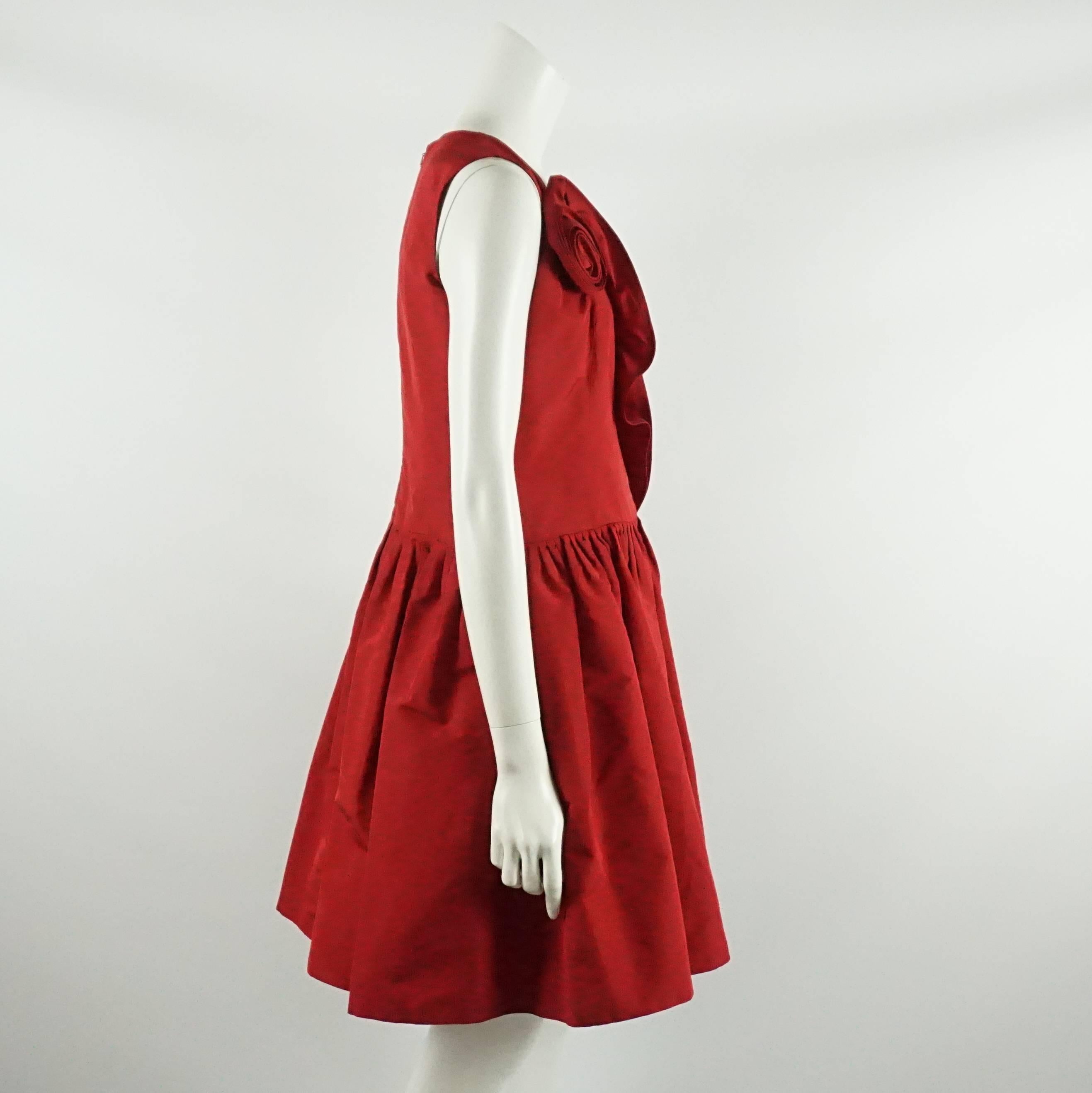 This Oscar de la Renta red silk taffeta dress is sleeveless with a drop waist and pleating at the beginning of the skirt. This dress also has a ruffle that leads into a rose along the bodice and going up to the bust. This dress is in excellent