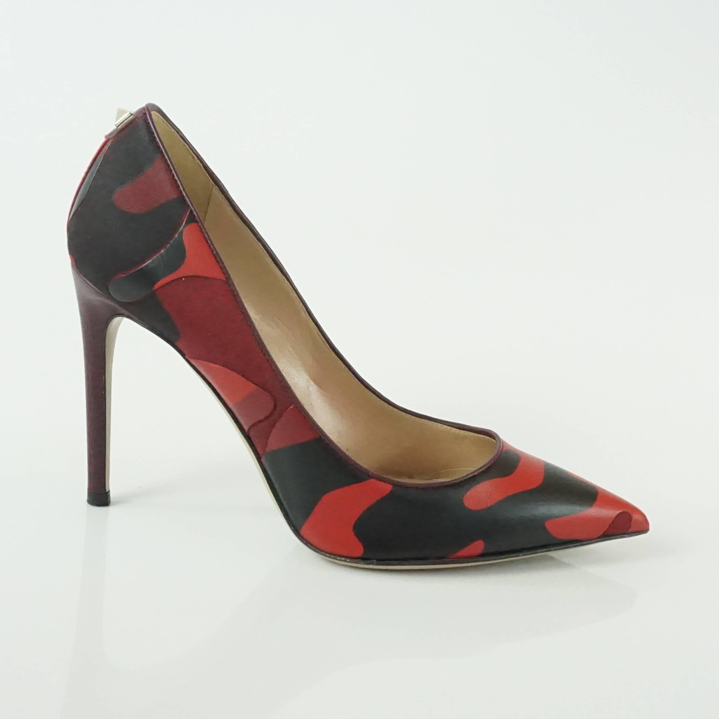 These Valentino pointed toe pumps are a red and black camo print made up of fabric and leather. The heel is a burgundy leather with one gold rockstud detail. They are in excellent condition with minor bottom wear and a very small light scuff on the