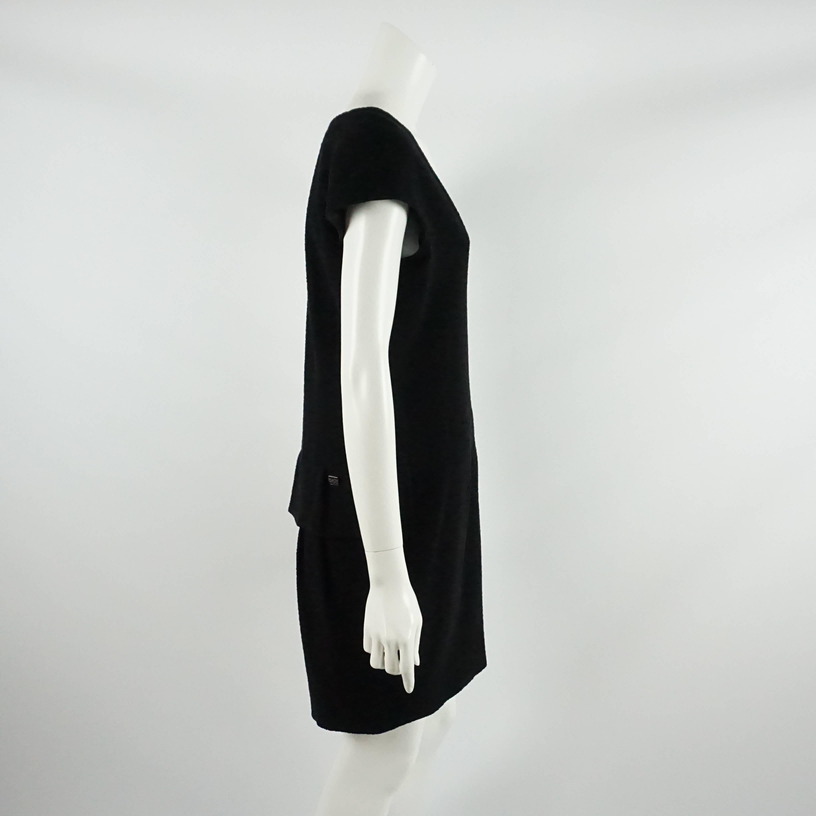 This Chanel black wool dress features a v-neck and a peplum in the back. On the peplum flap there is a rectangle with rhinestones and the Chanel logo. This dress is in excellent condition.