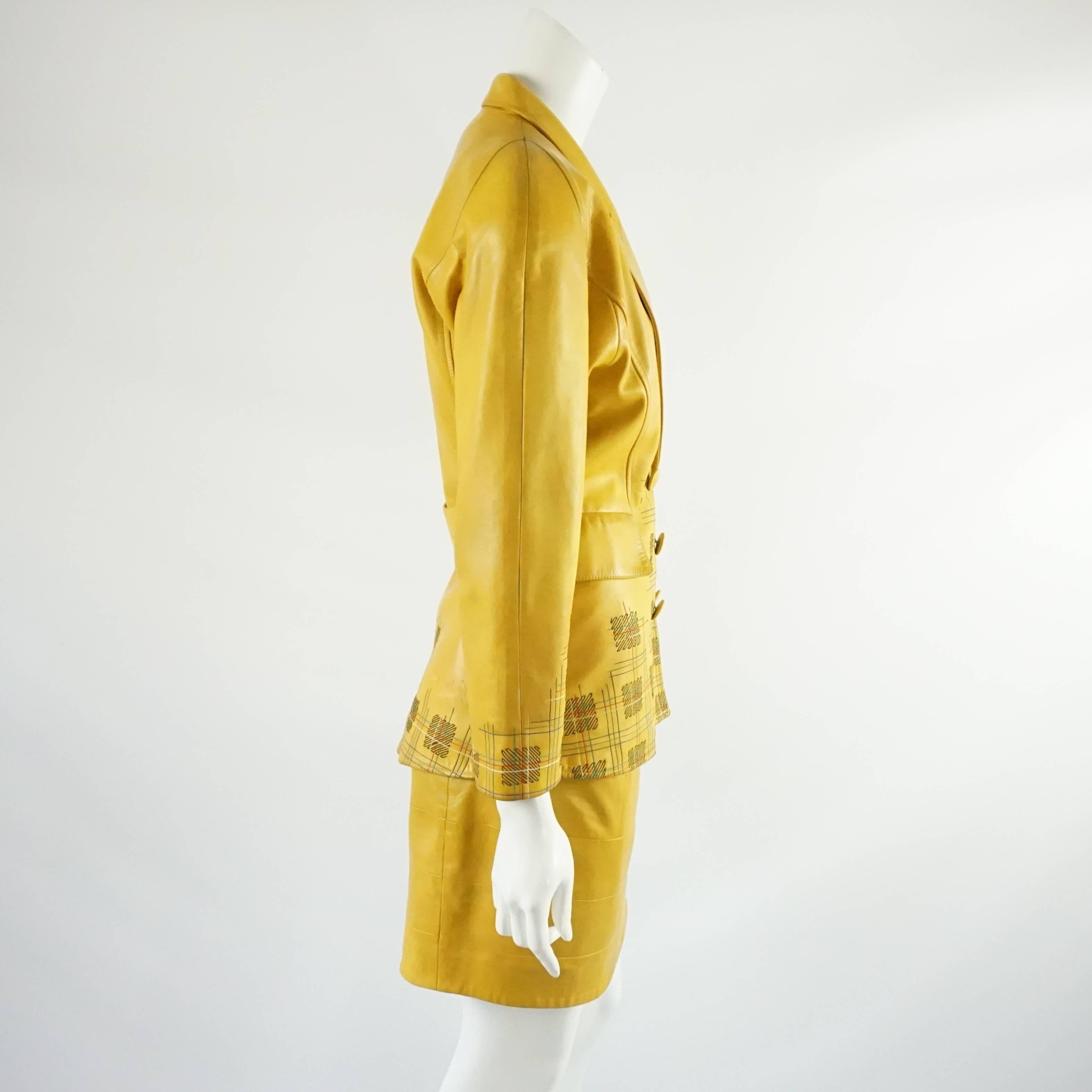 This vintage Jean Claude Jitrois yellow leather skirt suit has 6 buttons on the front of the jacket, 2 pockets, rounded shoulders, and 2 decorative buttons on the back. The jacket also has a design on the lower half that has black, red, green,
