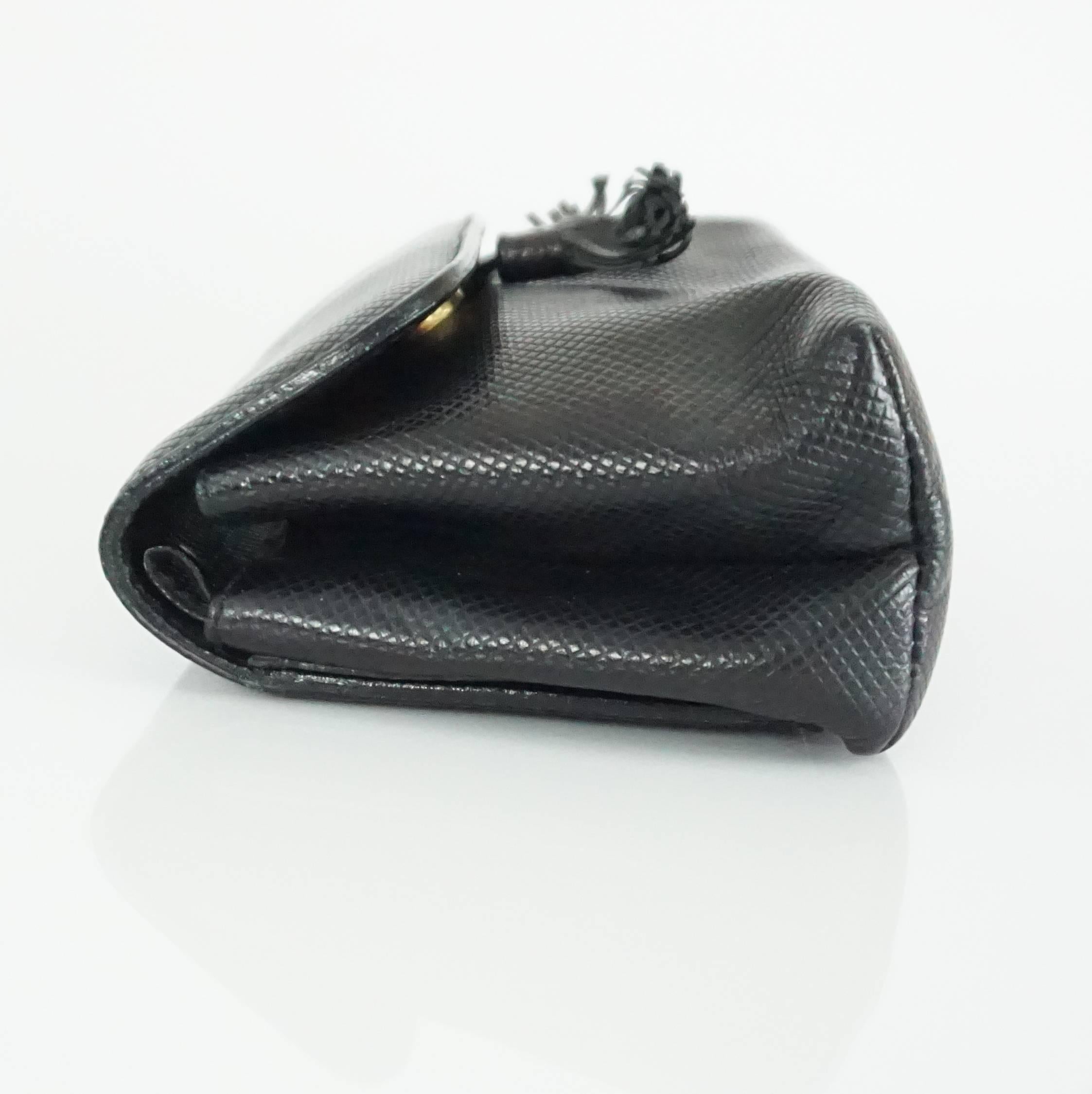 This Bottega Veneta small clutch is black embossed leather. There is a decorative tassel on the front, a snap closure, and an inside pocket. This clutch is in good condition with minor wear on a corner and the tassel being slightly frayed (see