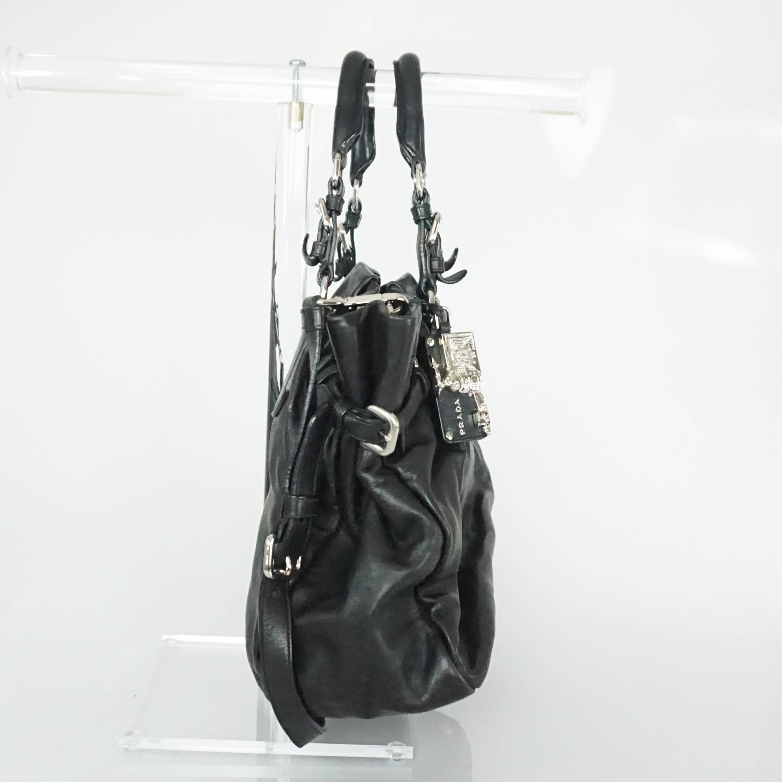 This Prada black leather shoulder bag has two handles and a crossbody strap. It has a silver logo, a silver and black leather rectangle charm, and a snap closure. It is in very good condition with minor wear to the handle.

Measurements
Height: