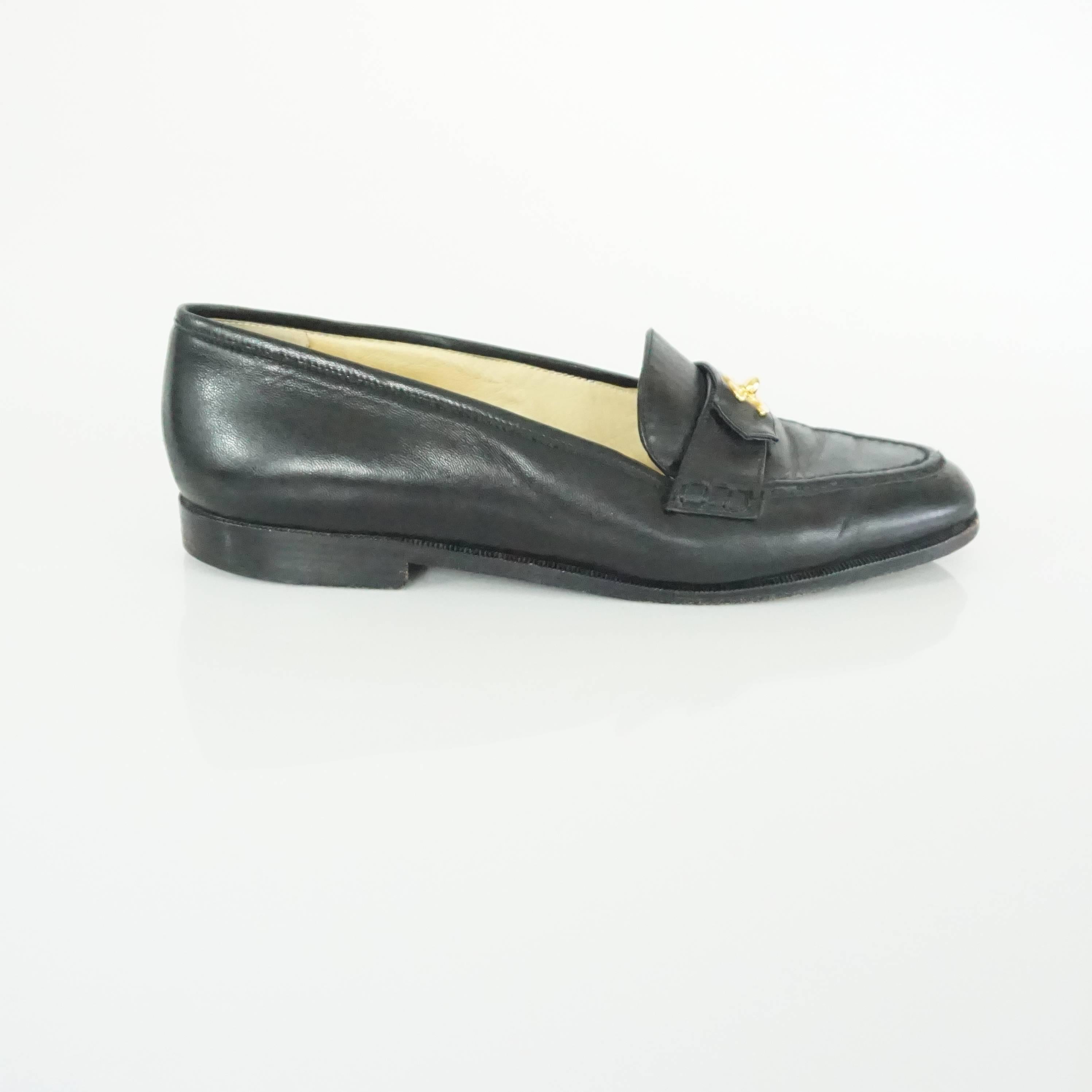 These Chanel black leather loafers feature a gold "CC" turnkey detail on the front. They are in good condition with bottom wear and some scuffing.
