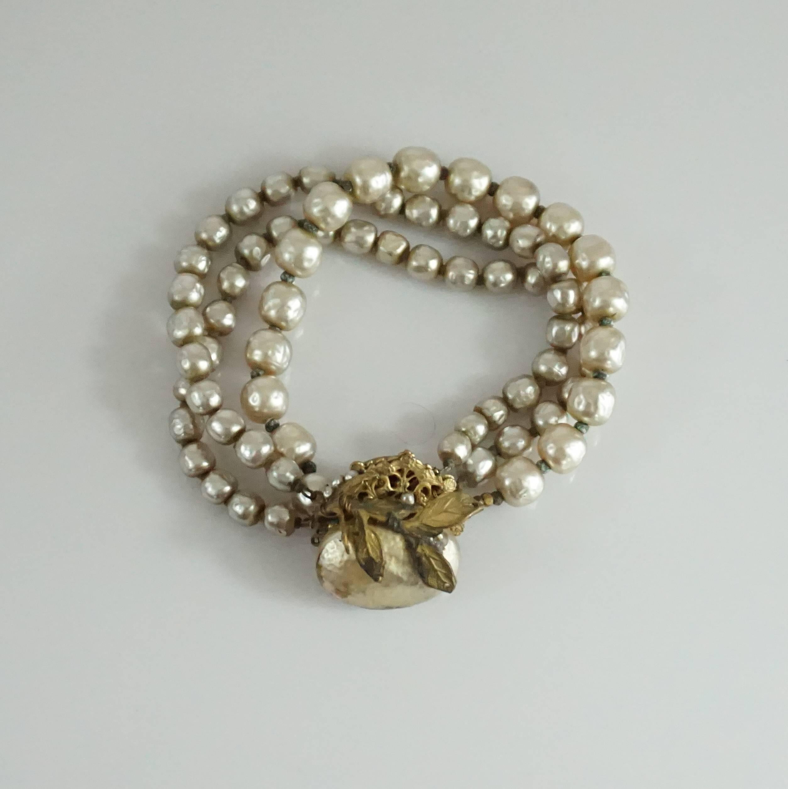 This Miriam Haskell cream pearl bracelet has 3 strands of pearls. It has a large center pearl with a gold leaf that is the clasp of the bracelet. The bracelet is in fair vintage condition with some general chipping to the strands, chipping on the