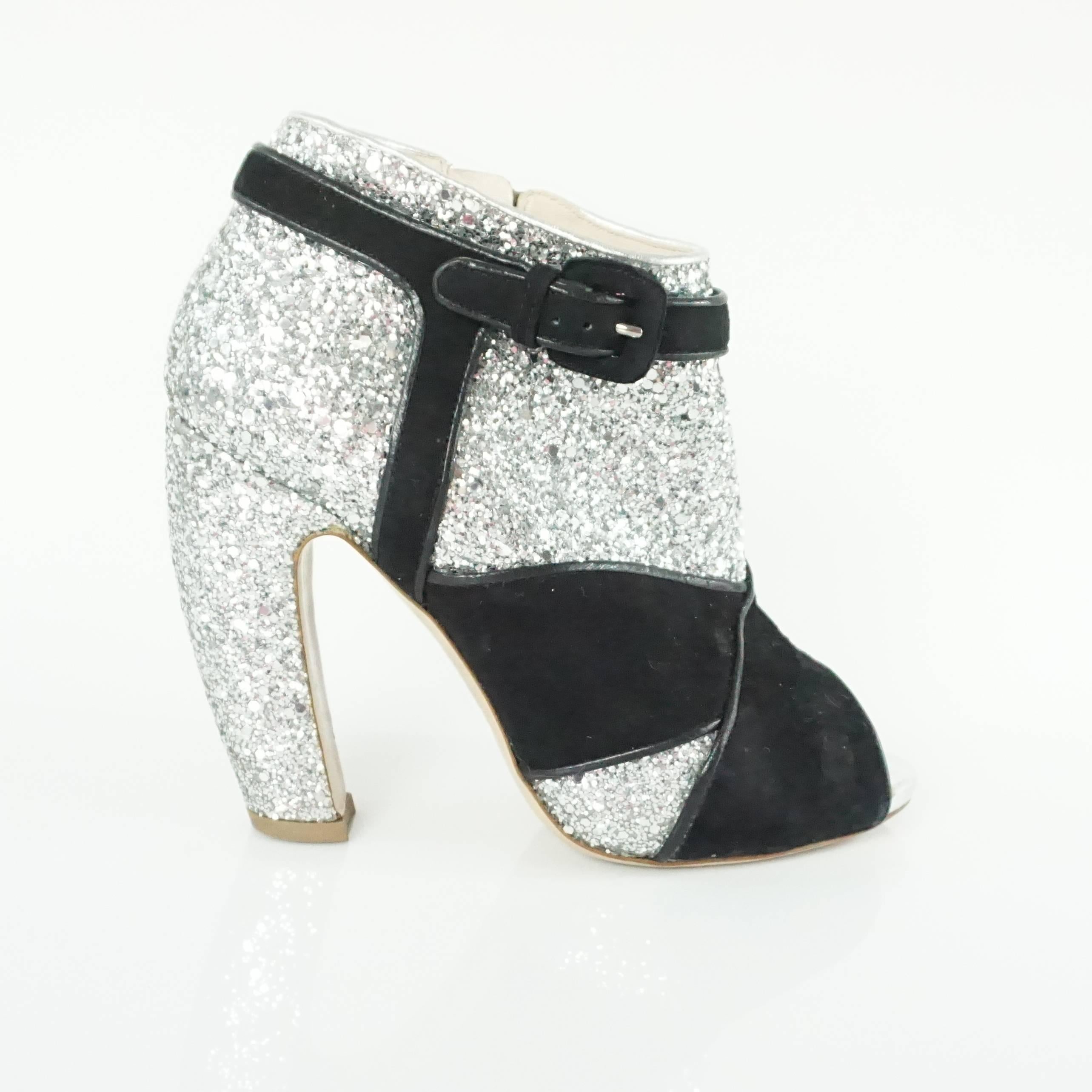 These Miu Miu booties are a truly spectacular find. They feature a silver glitter body with black suede overlay in the shape of a vintage heel. The booties also have a back zip and peep toes. They are in good condition with general wear to the body