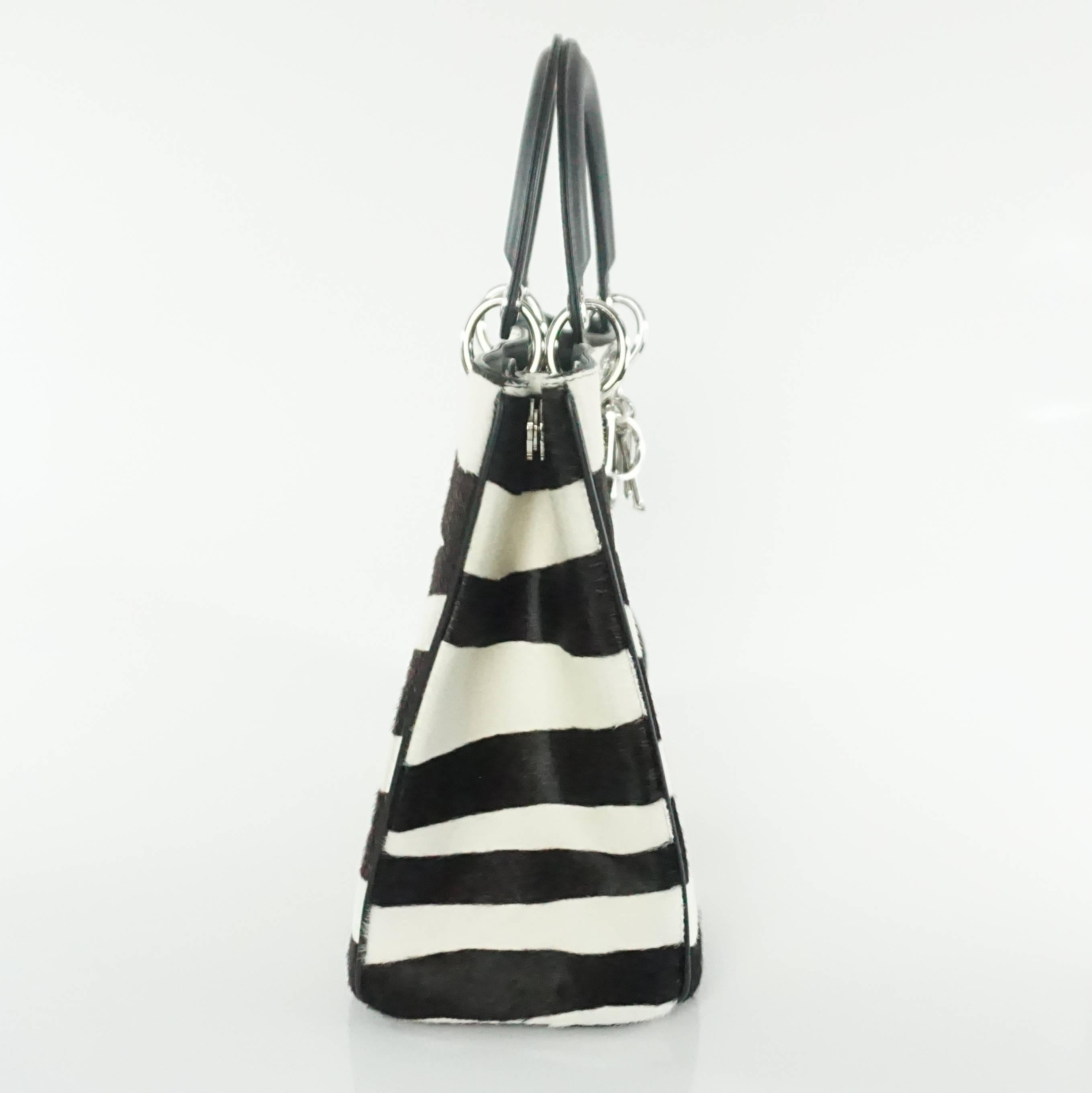 This Dior pony hair bag is a fabulous piece. It features a dark brown and ivory pony hair fabric, black leather handles and trim, and silver hardware with a hanging logo chain. The bag has a black leather lining and comes with a small black case,