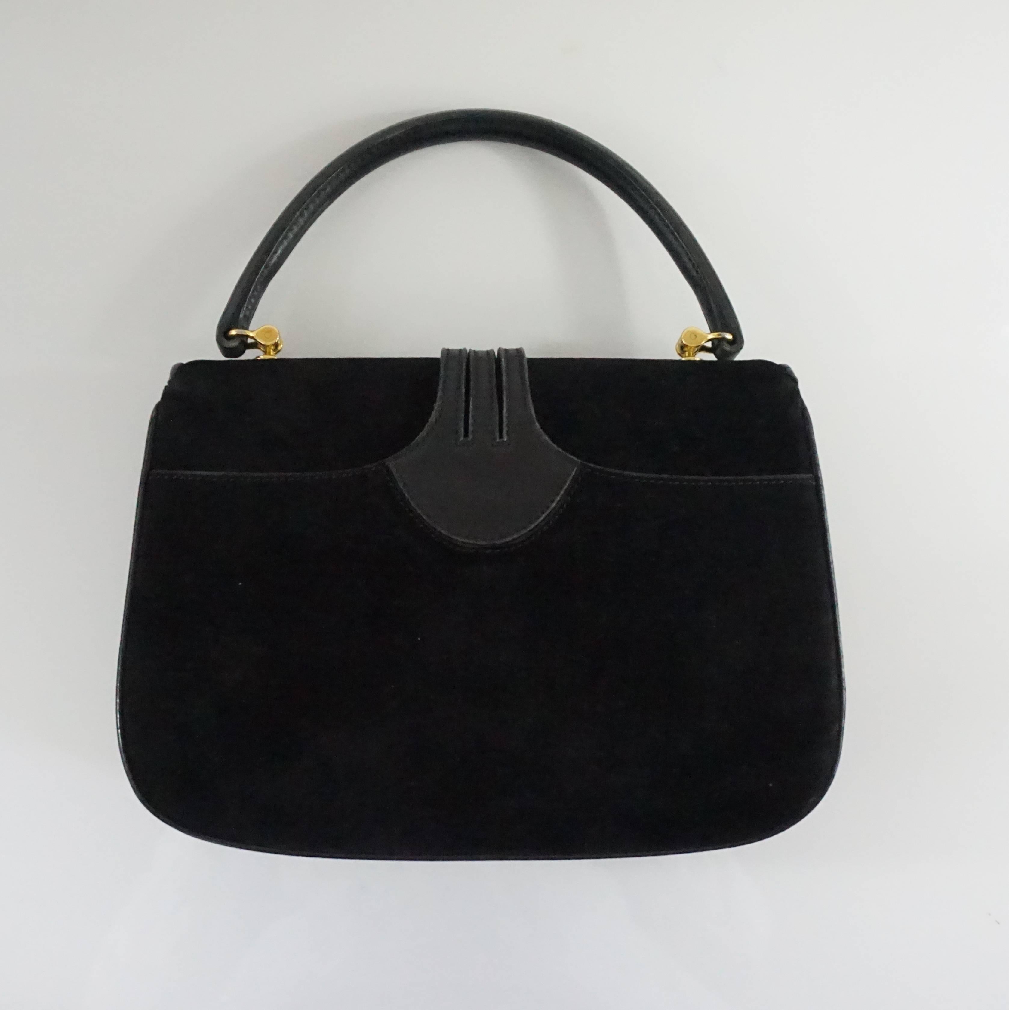 This vintage Gucci black suede bag has a leather top handle and leather detailing. It has gold hardware and a duster is included. This bag is in very good vintage condition with some wear to the hardware and
