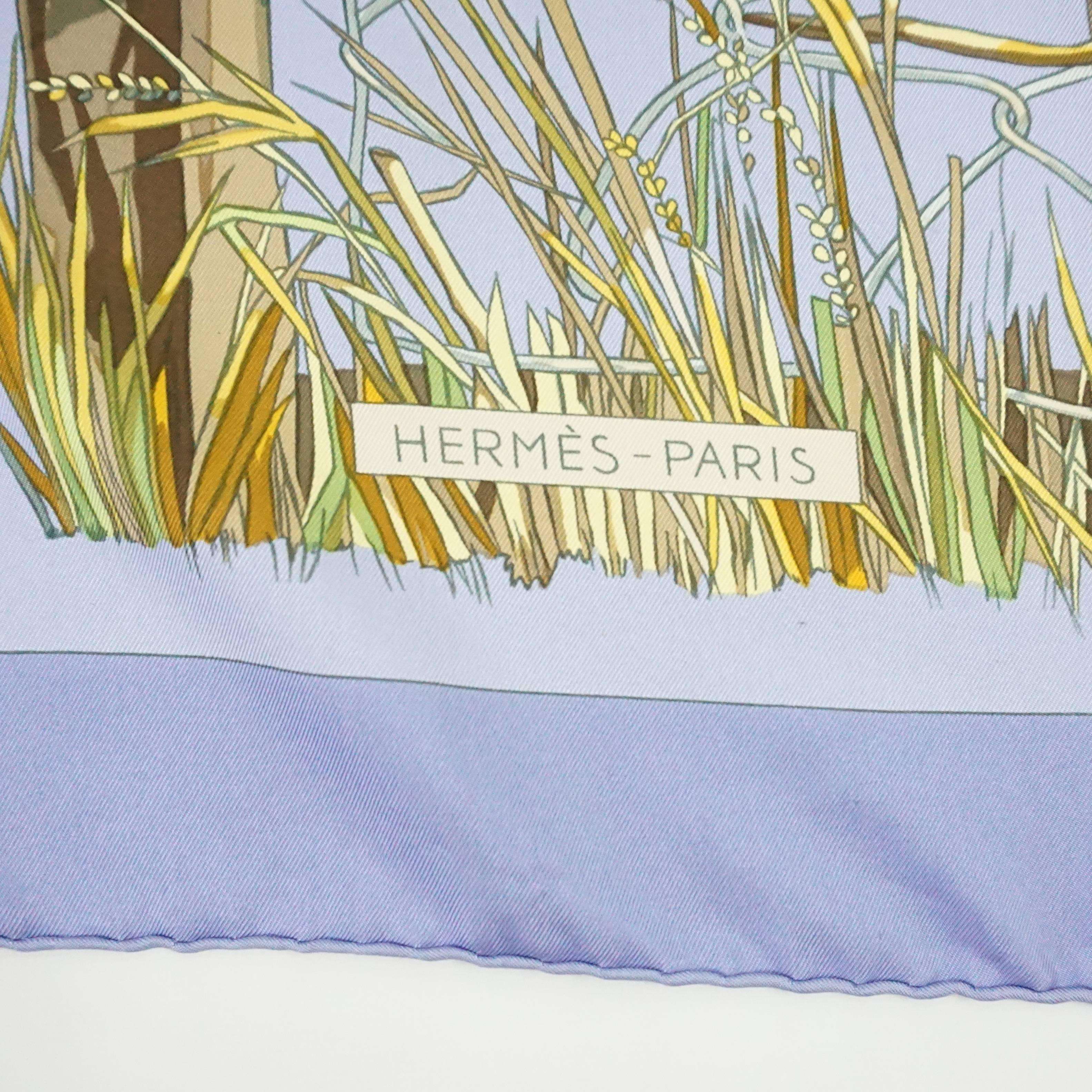 This Hermes silk scarf has mainly periwinkle on it with a lavender trim. The print is of a prairie-like fence with different motifs on it. It is by Francoise Heron and is titled, 