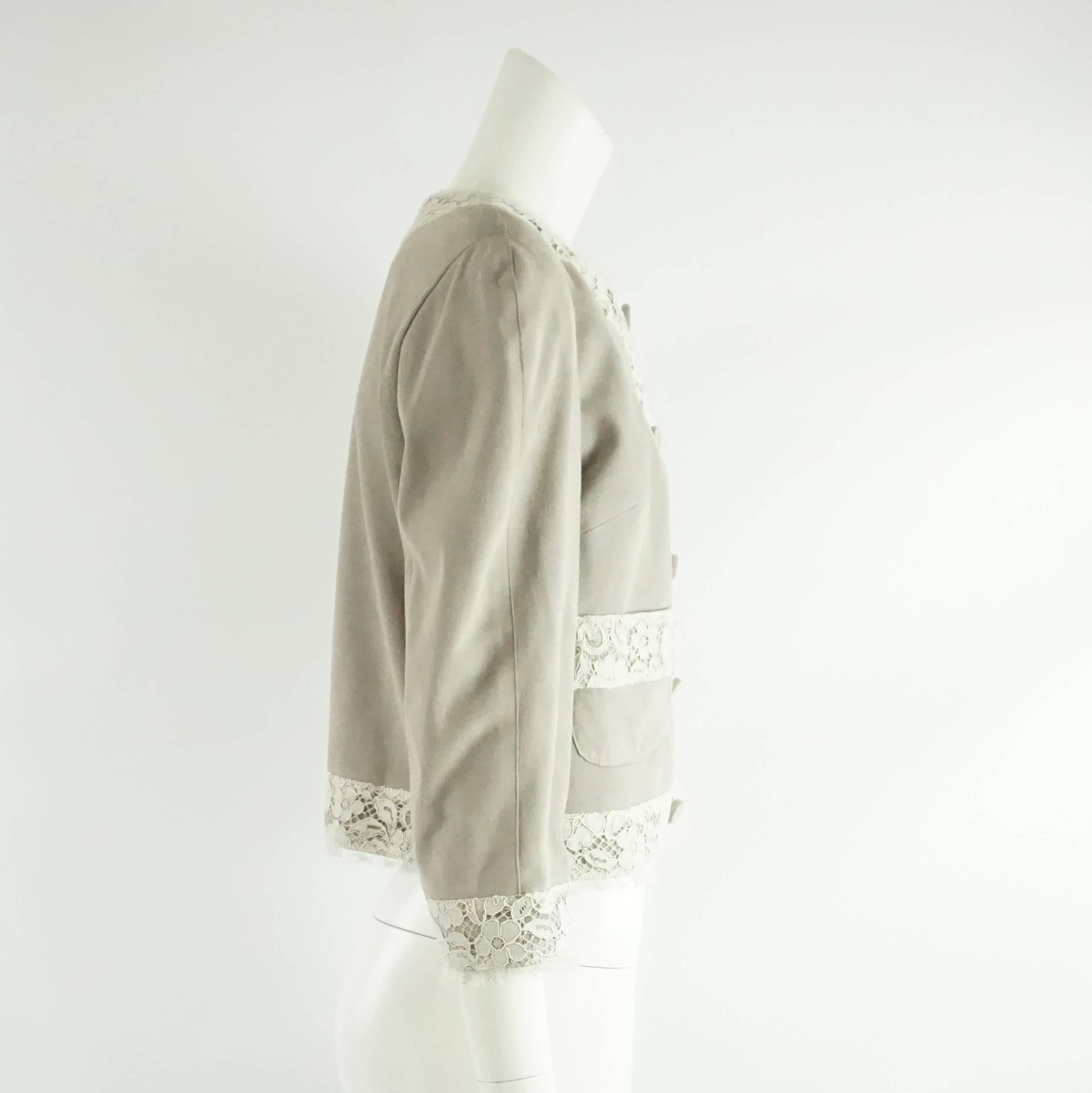 This Dolce & Gabbana jacket is gray suede and has an ivory lace trim. The jacket is lined in a Black and White Silk Polka Dot fabric and has a 3/4 sleeve. There are 2 front pockets and 5 large suede covered Snap buttons. This jacket is in very good