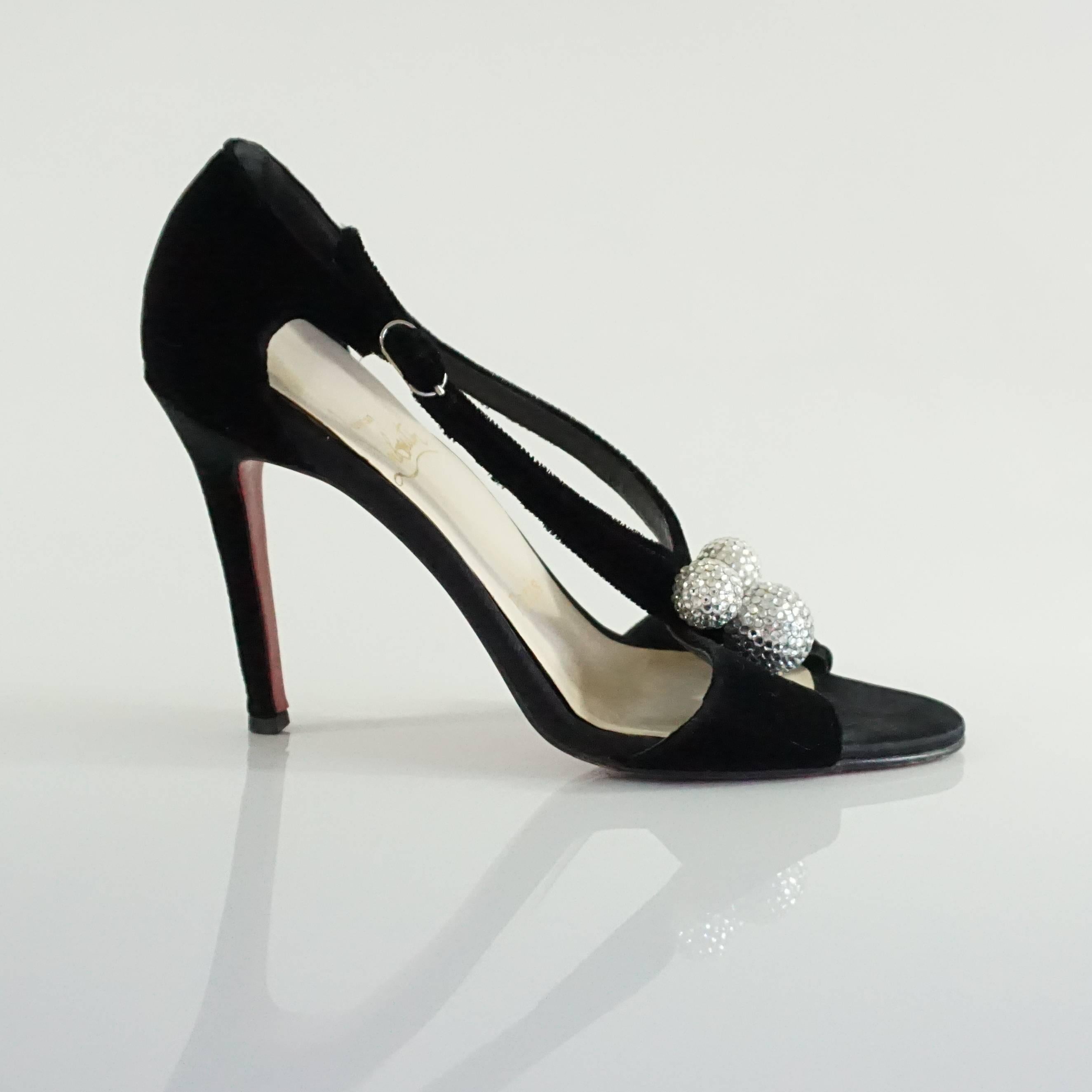 These Christian Louboutin sandals are black velvet and have 3 rhinestone covered balls on the front of them. They feature an open toe and straps that close around the ankle. They are in good condition with some wear on the bottom and toe bed and the