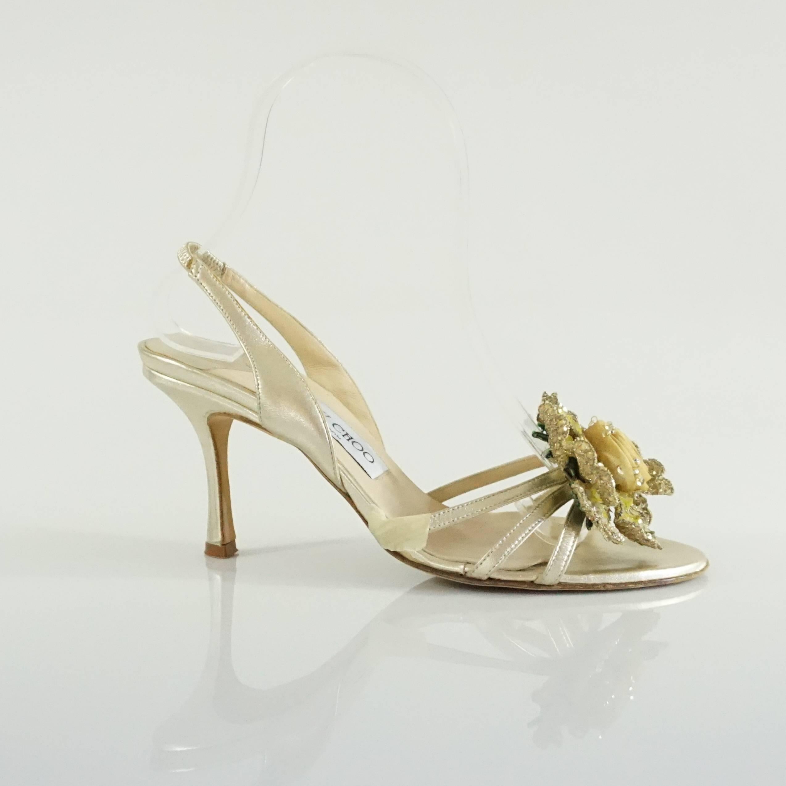 These gold Jimmy Choo leather sandals have a slingback and an open toe. On the toe, there is a rose detail. These shoes are in good condition with some bottom wear and markings on the heels.

Heel Height: 3