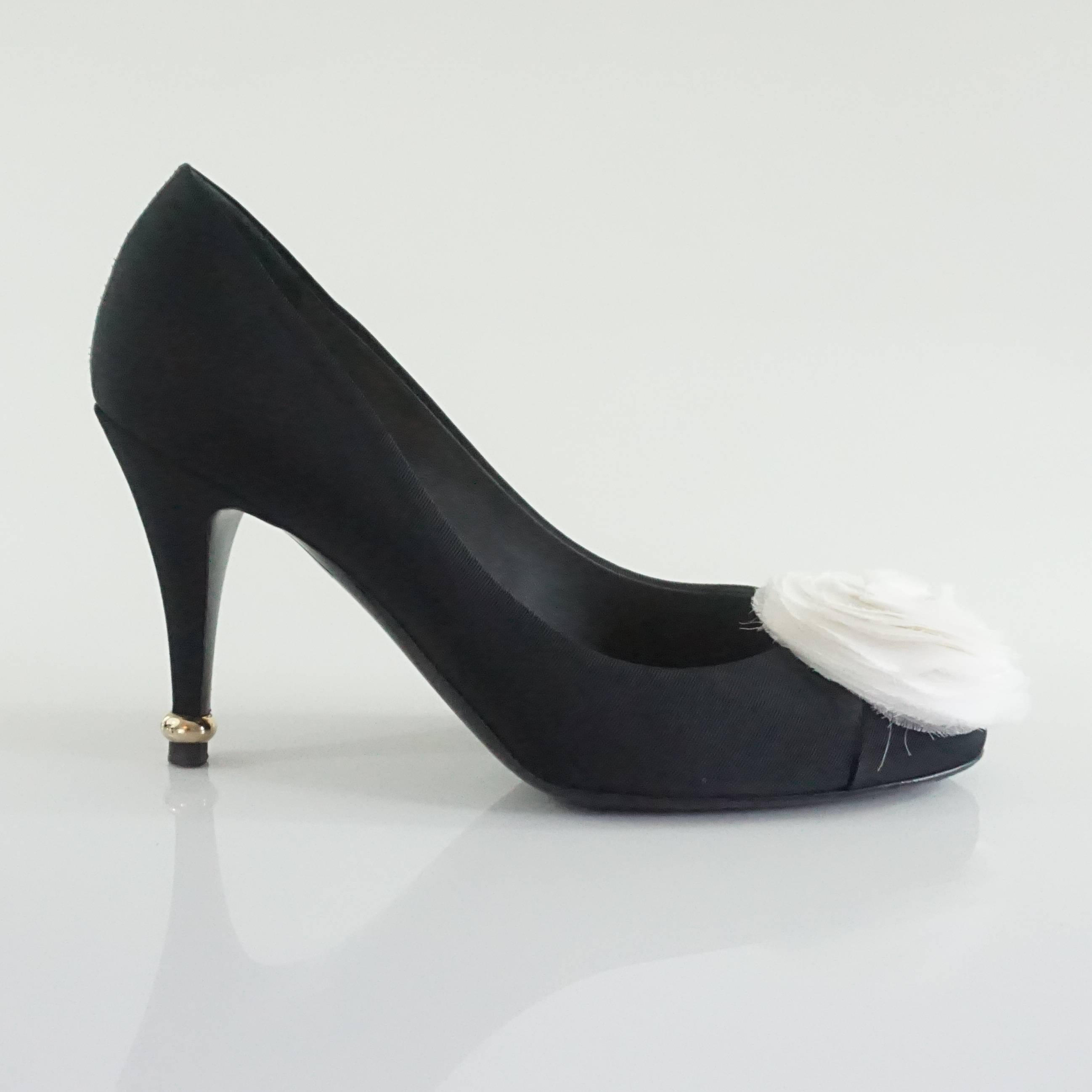 The beautiful Chanel black grosgrain pumps have an ivory silk camellia on the toe. There is a small silver detail with "Chanel" engraved on the heel. These shoes are very good condition with some minor wear on the bottom. 

Heel Height: