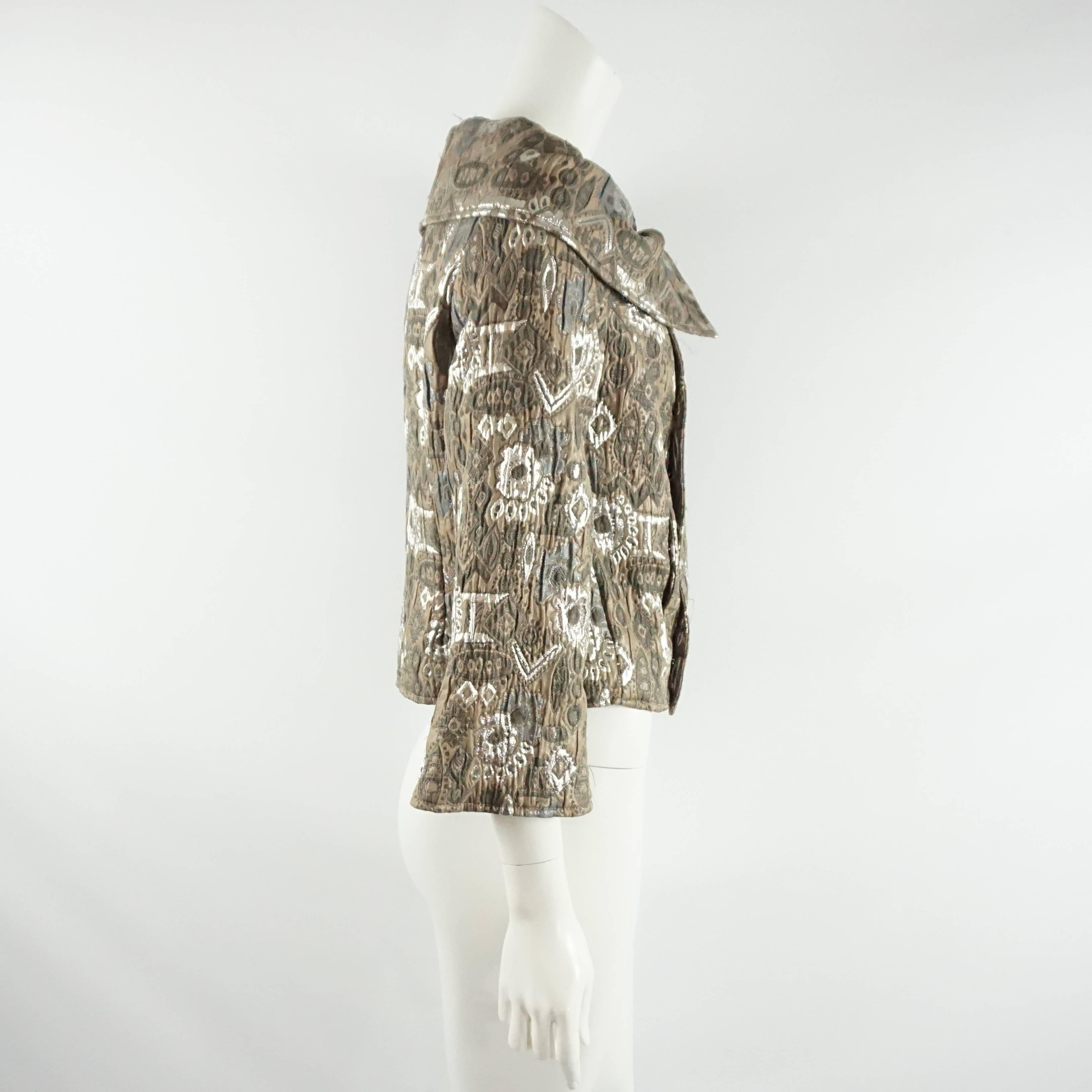 This stunning Oscar de la Renta taupe jacket is made of a polyester-silk blend brocade fabric that has silver metallic in it. The jacket is double breasted and has a slouchy portrait collar, a swing look, and 2 front pockets. It is in good condition