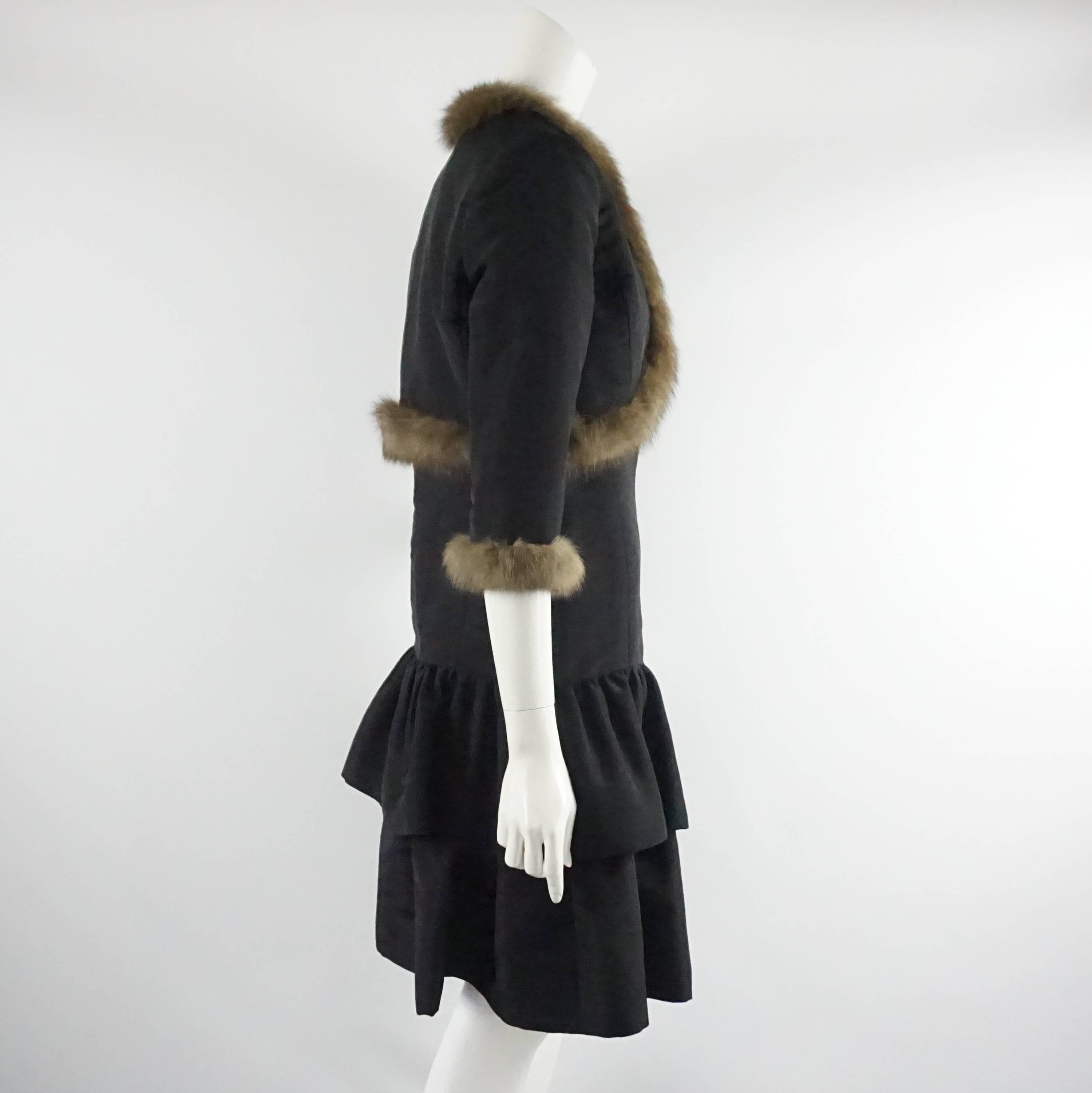 Este vestido negro de tafetán de Oscar De La Renta es sin tirantes, con cintura caída y dos volantes inferiores. La chaqueta a juego es un bolero recortado con manga 3/4 y ribete de marta. Ambas piezas están en excelente estado, con un desgaste