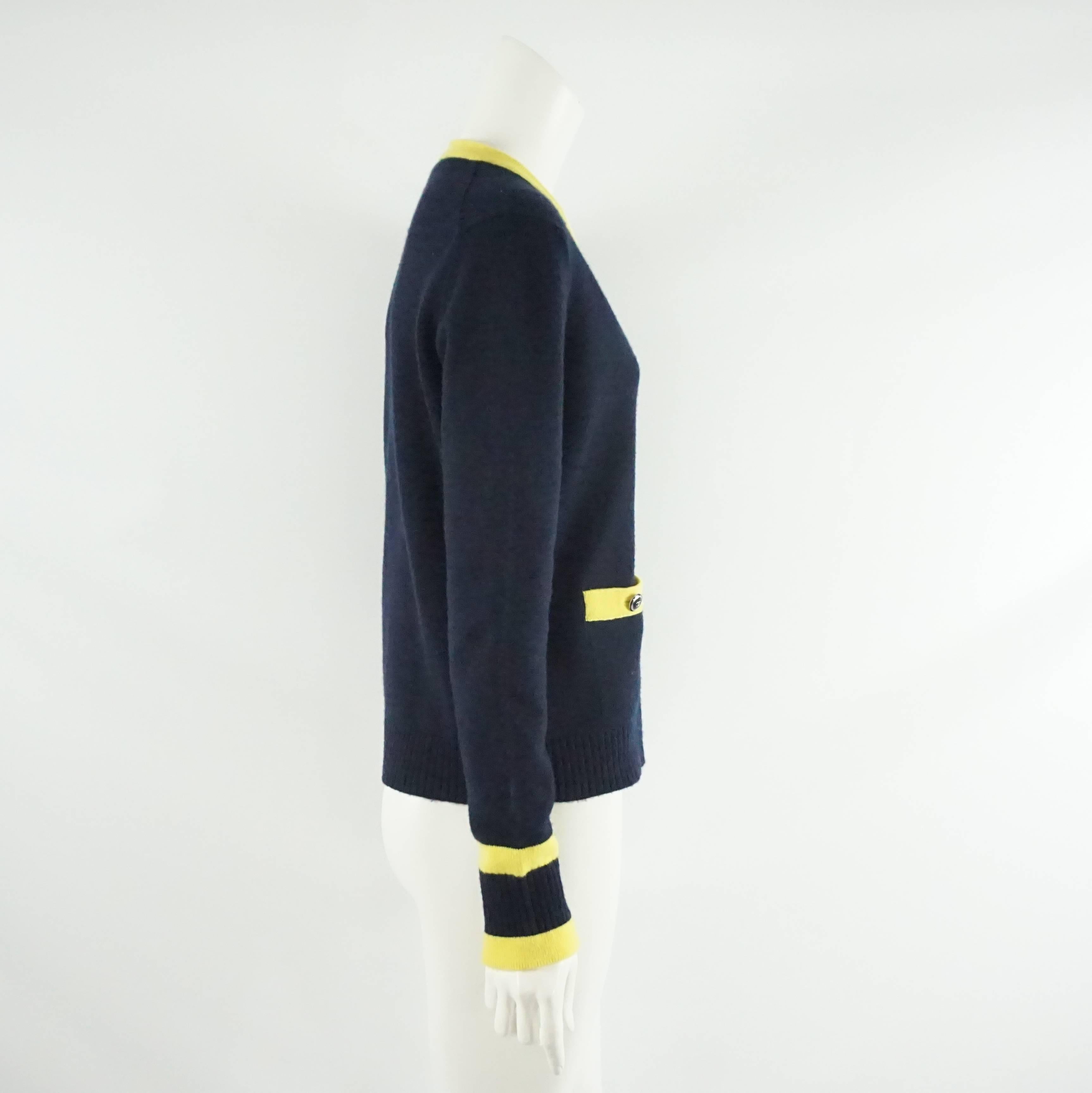 This Chanel cashmere sweater is navy with a yellow trim. The buttons are a dark gray and there are 2 pockets on the front. At the bottom of the sleeves there are 2 yellow stripes. This sweater is in very good condition with minor