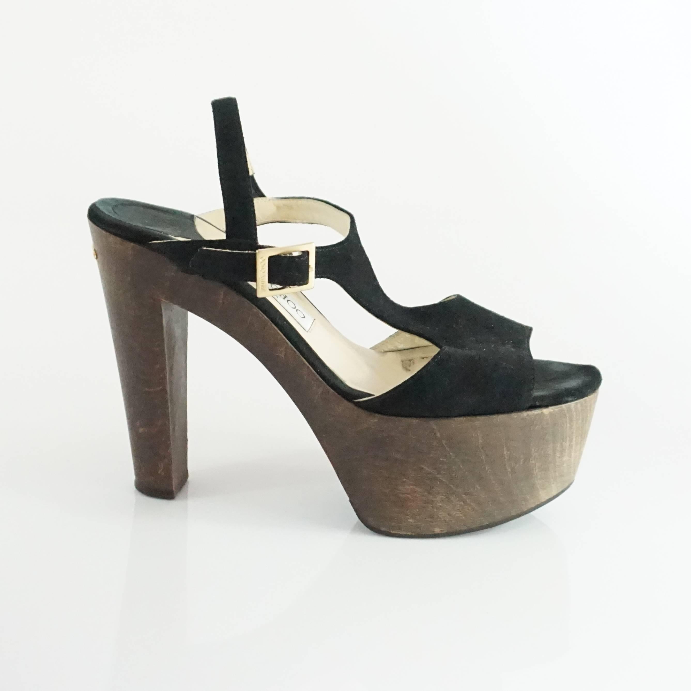 These Jimmy Choo platform heels are show stoppers. They are made of black suede and have a t-strap, wooden platform and heel, and Jimmy Choo logo plaque in the back. They are in fair condition with some small marks on the wood platform and wear on