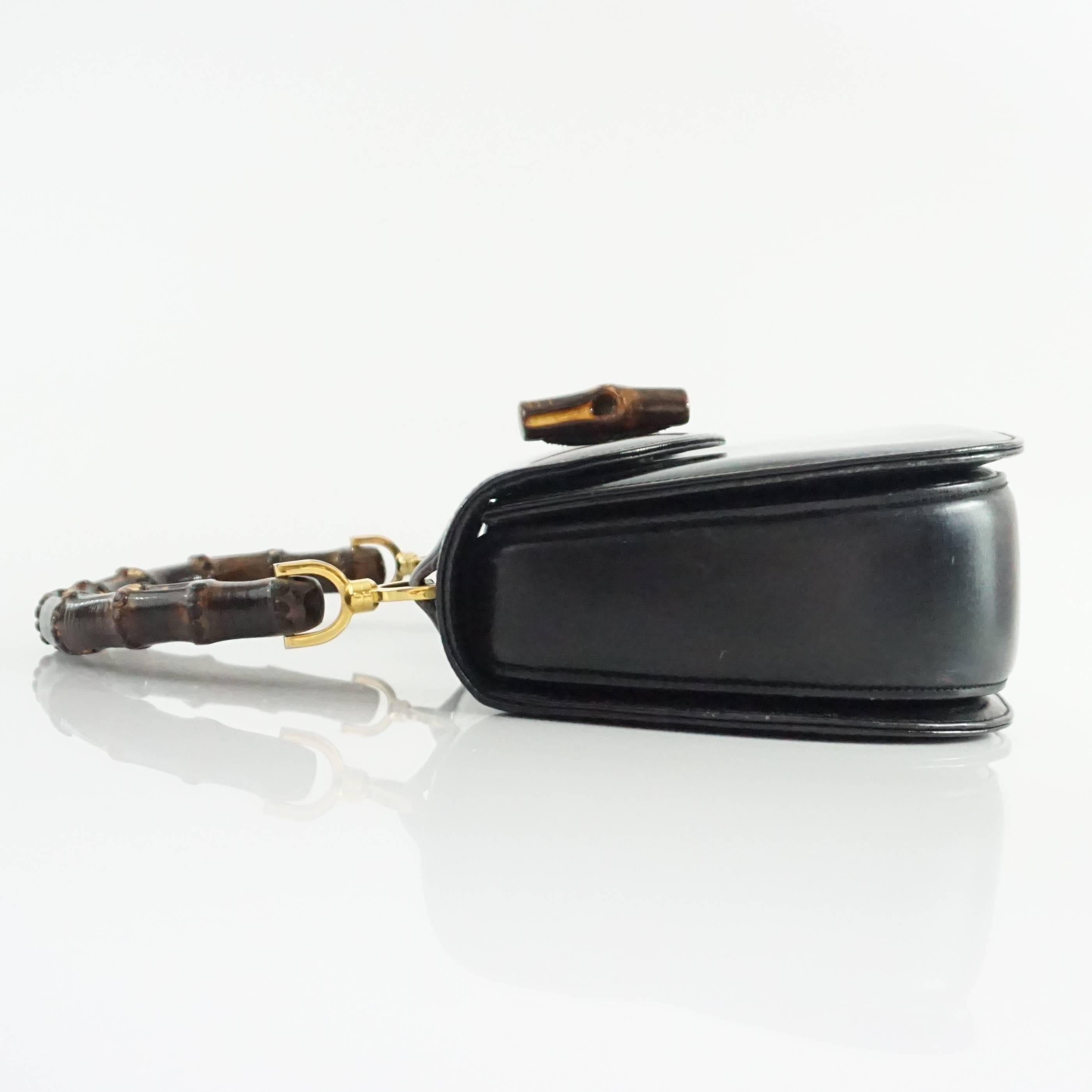 This vintage Gucci top handle bag is black leather with a bamboo handle and closure. On the inside, there is a zippered pocket, an open pocket, and a pocket with a snap closure. There is gold hardware in addition to the bamboo handle. The bag is in