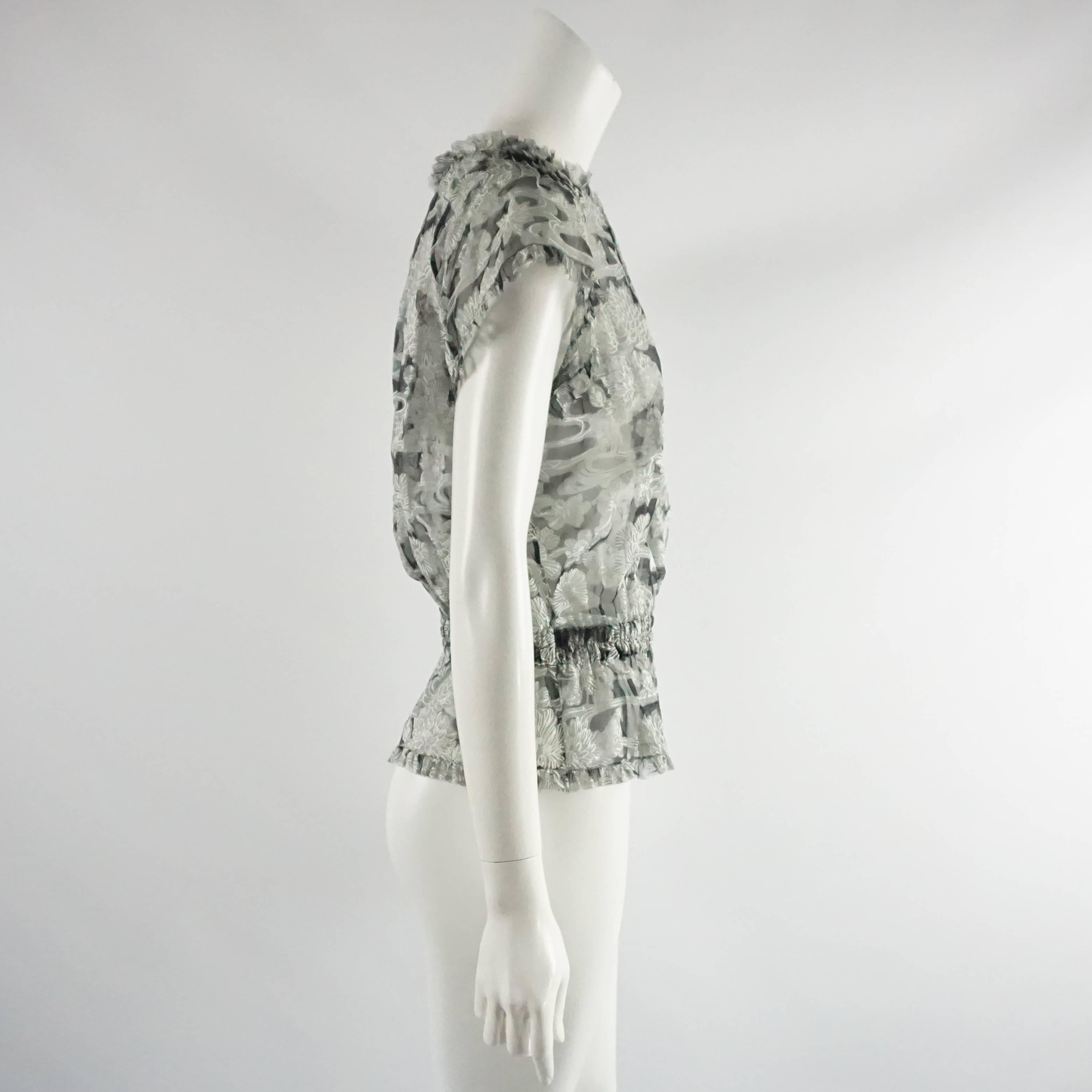 This Chanel silk chiffon top is gray with a floral print. The top cinches towards the bottom and then flares out. There is a small textured silver and black metal button on the back along with a keyhole opening. This top features short sleeves and a