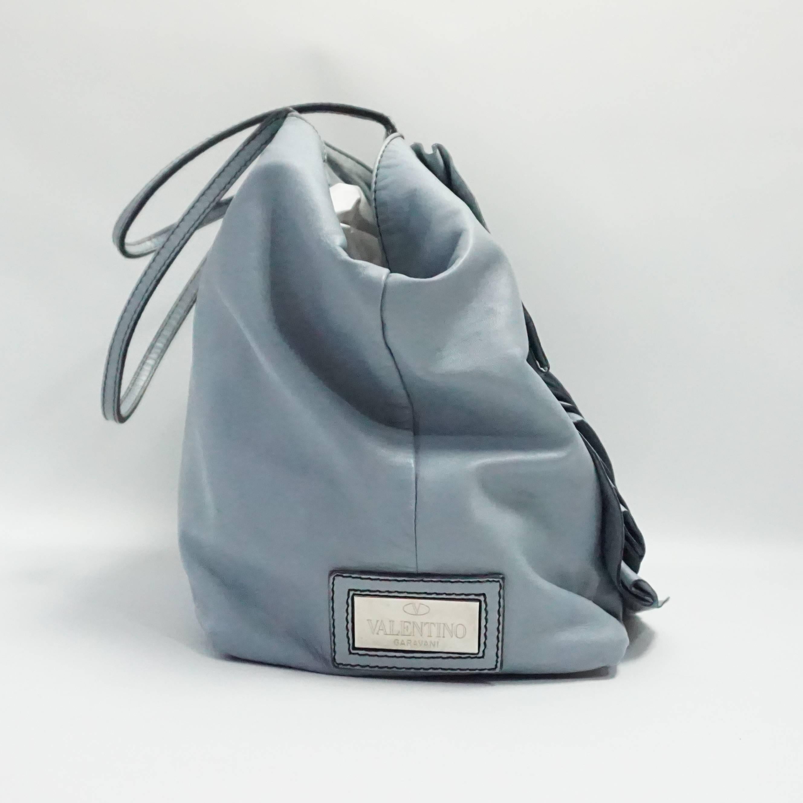 This Valentino Petale Rose tote is pale blue leather. It is large and has two straps along with a detachable shoulder strap. This tote is in very good condition with some staining inside and outside. This tote retails for