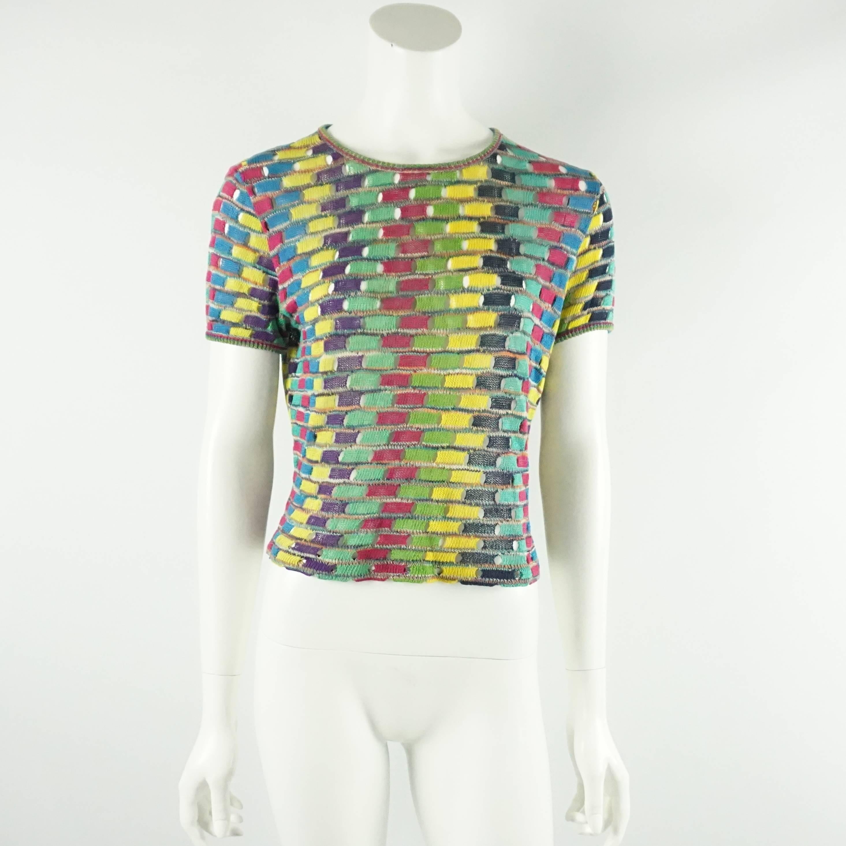 This vintage Missoni sweater set has a multi colored pattern on both the top and the sweater. The sweater has long sleeves and clear lucite buttons. The top has short sleeves and a rounded neckline. Both pieces are in excellent vintage