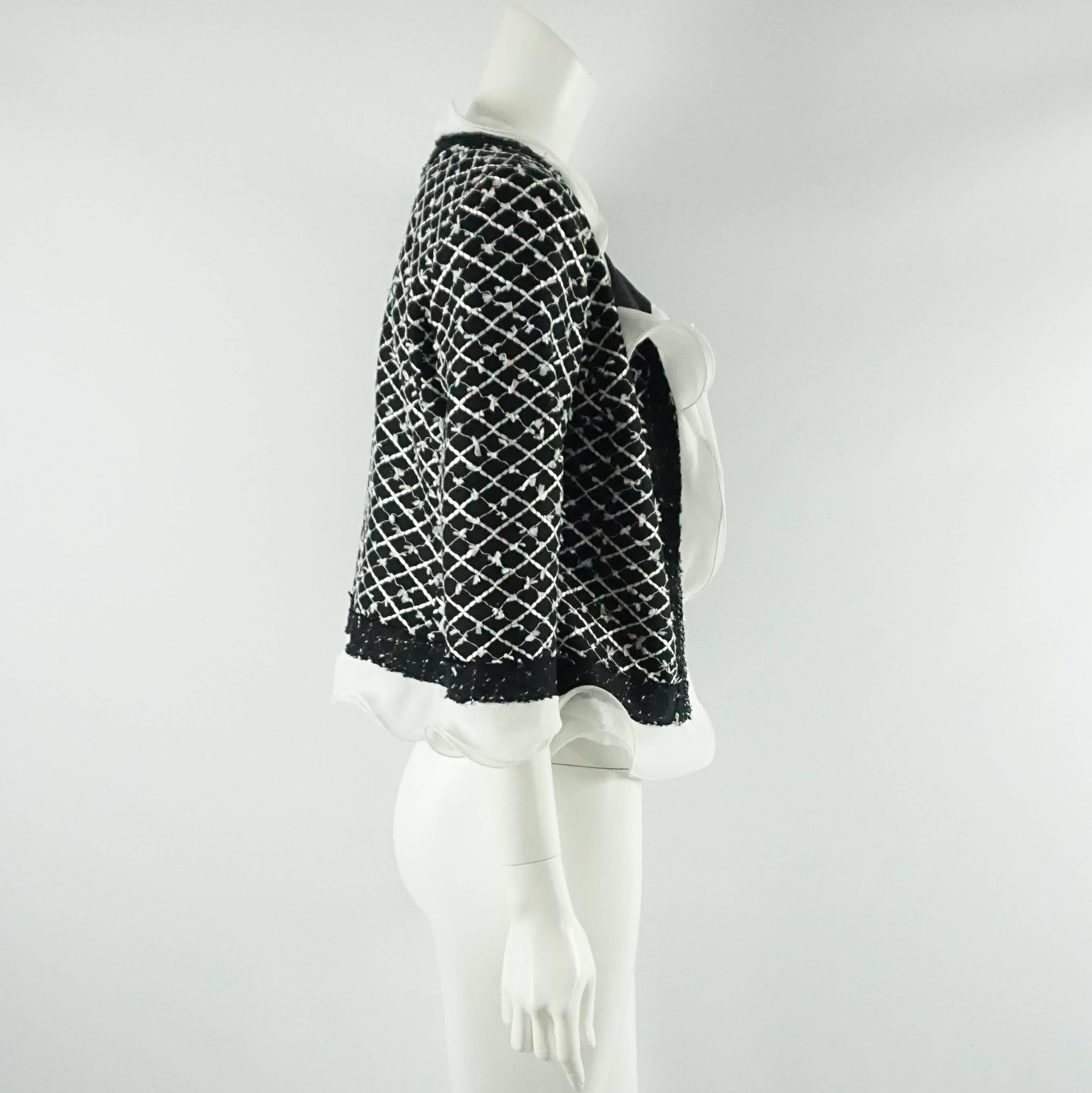 This Oscar de la Renta black and white tweed jacket is a classic staple. It has a fringe and silk chiffon ruffle trim all around with no closure in the front. The fabric is a cotton-synthetic blend with silk lining. There are also very thin shoulder