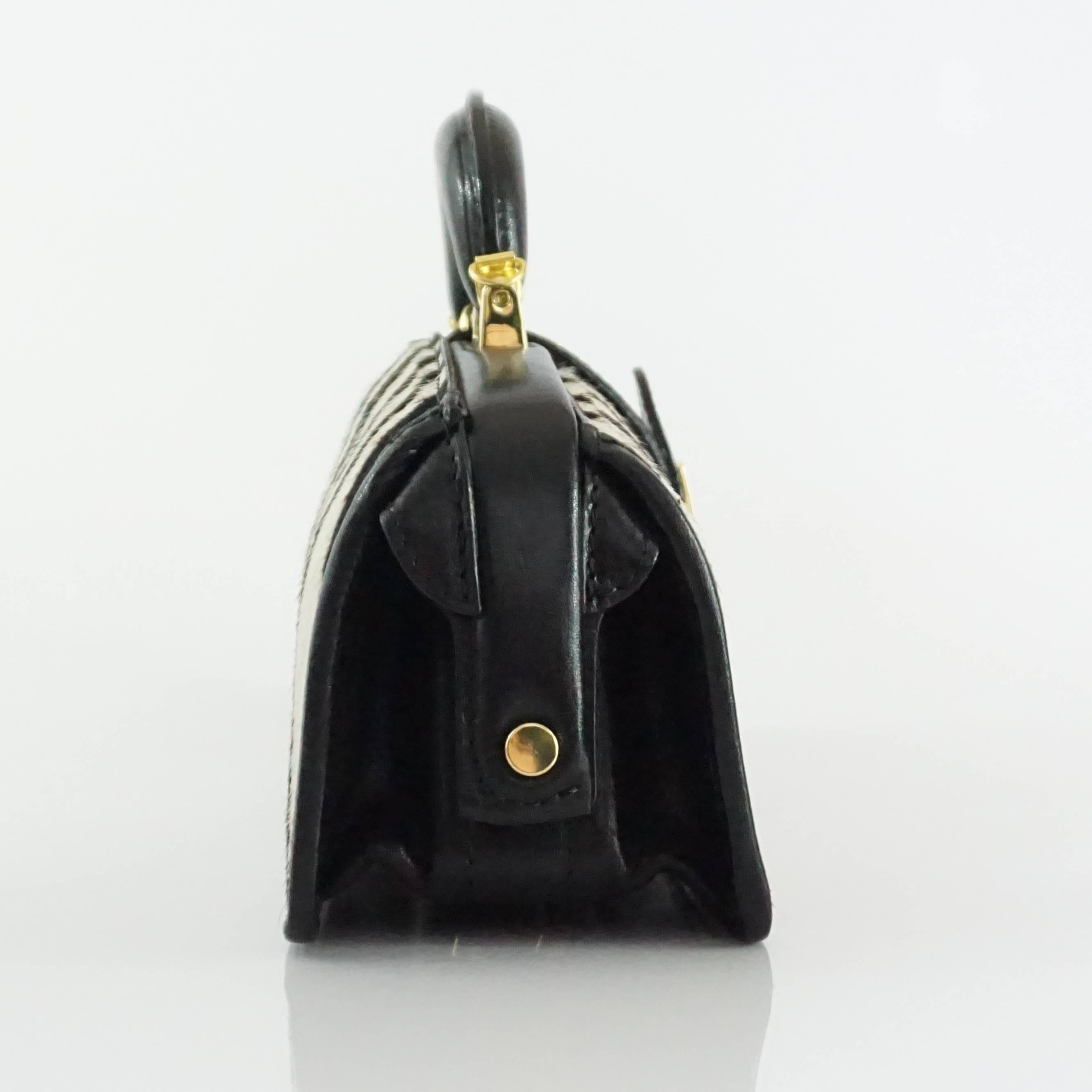 This Pratesi handbag is black and white pony hair with a black handle. It features a gold closure with a gold key inside. There is also a built in light inside which allows you to see the bag's contents at night. This bag is in excellent