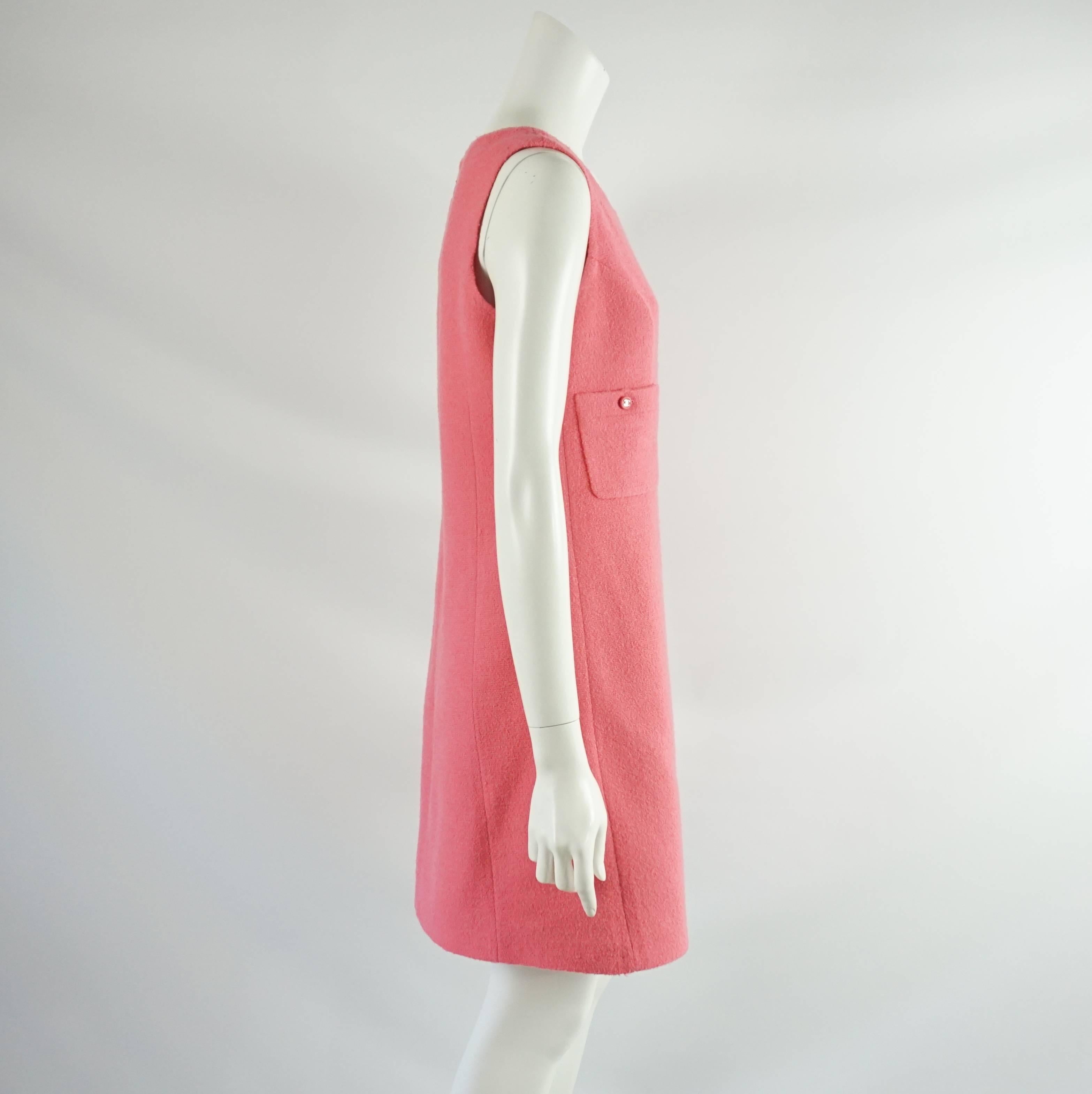 This beautiful Chanel sleeveless dress is pink wool. There are 2 front pockets with 2 buttons, both pink with a silver Chanel logo. This piece is very good condition with paint chipped on the zipper and interior underarm staining. Size 8, circa