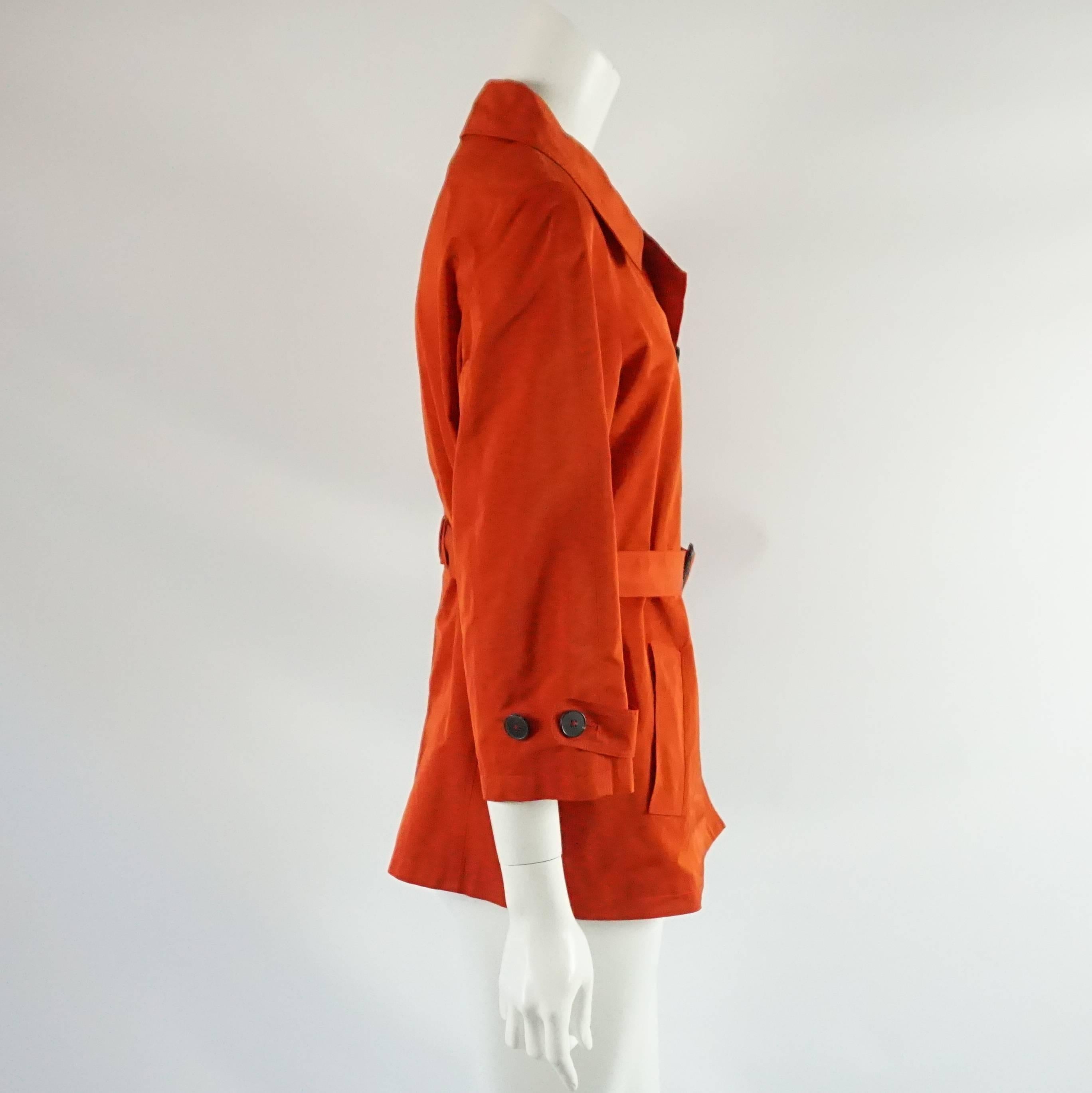 This beautiful Jil Sander long jacket is red silk blend. It has 6 buttons going down the front and two buttons on each sleeve. There is a belt with a buckle that matches the buttons. There are two pockets on the front. This jacket is in very good