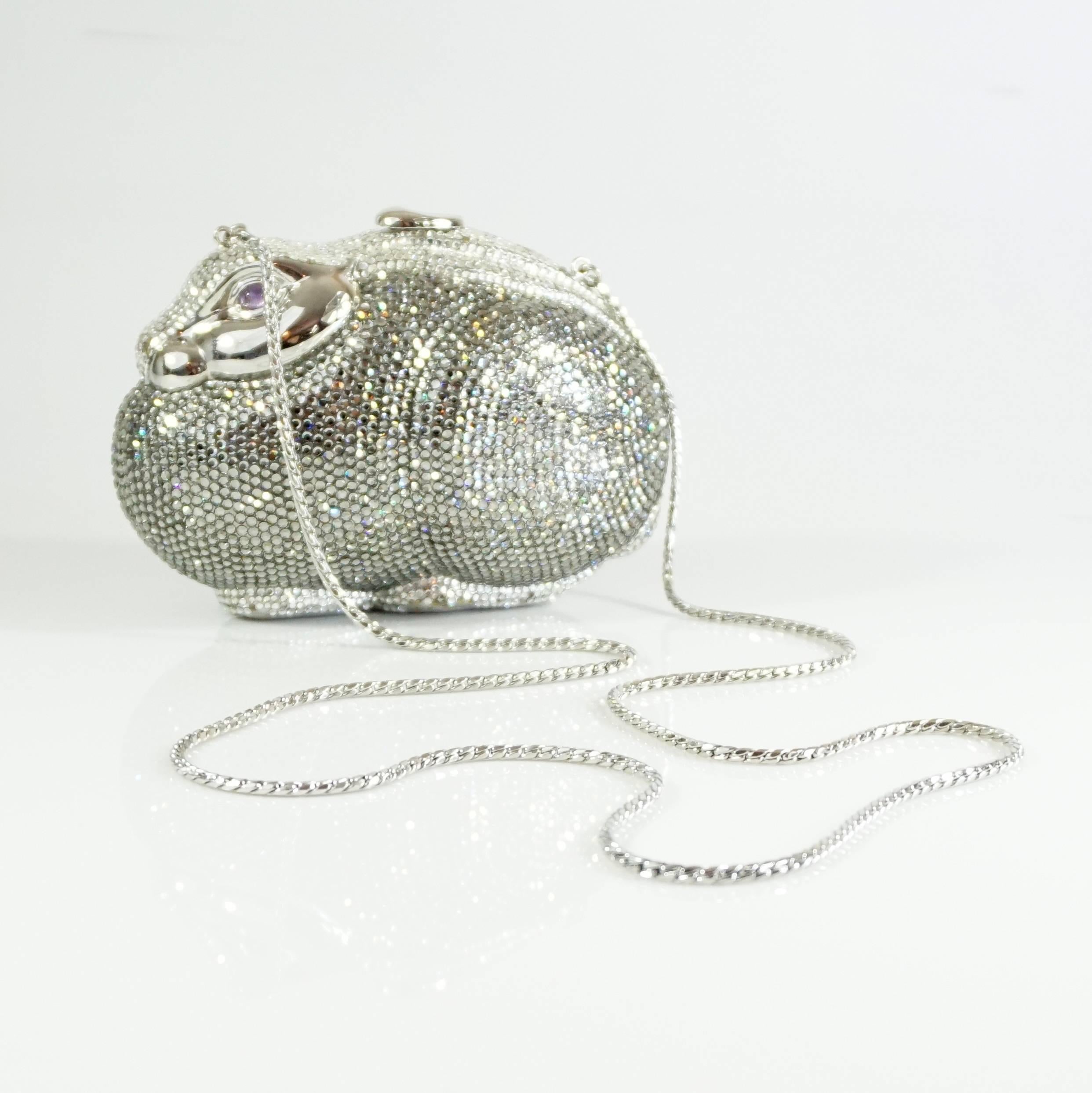 This Judith Leiber minaudiere has different tones of silver rhinestones with purple stone eyes on silver metal. It is in the shape of a bunny rabbit and has a longer crossbody strap which can be hidden. Purchase comes with a duster, comb, compact