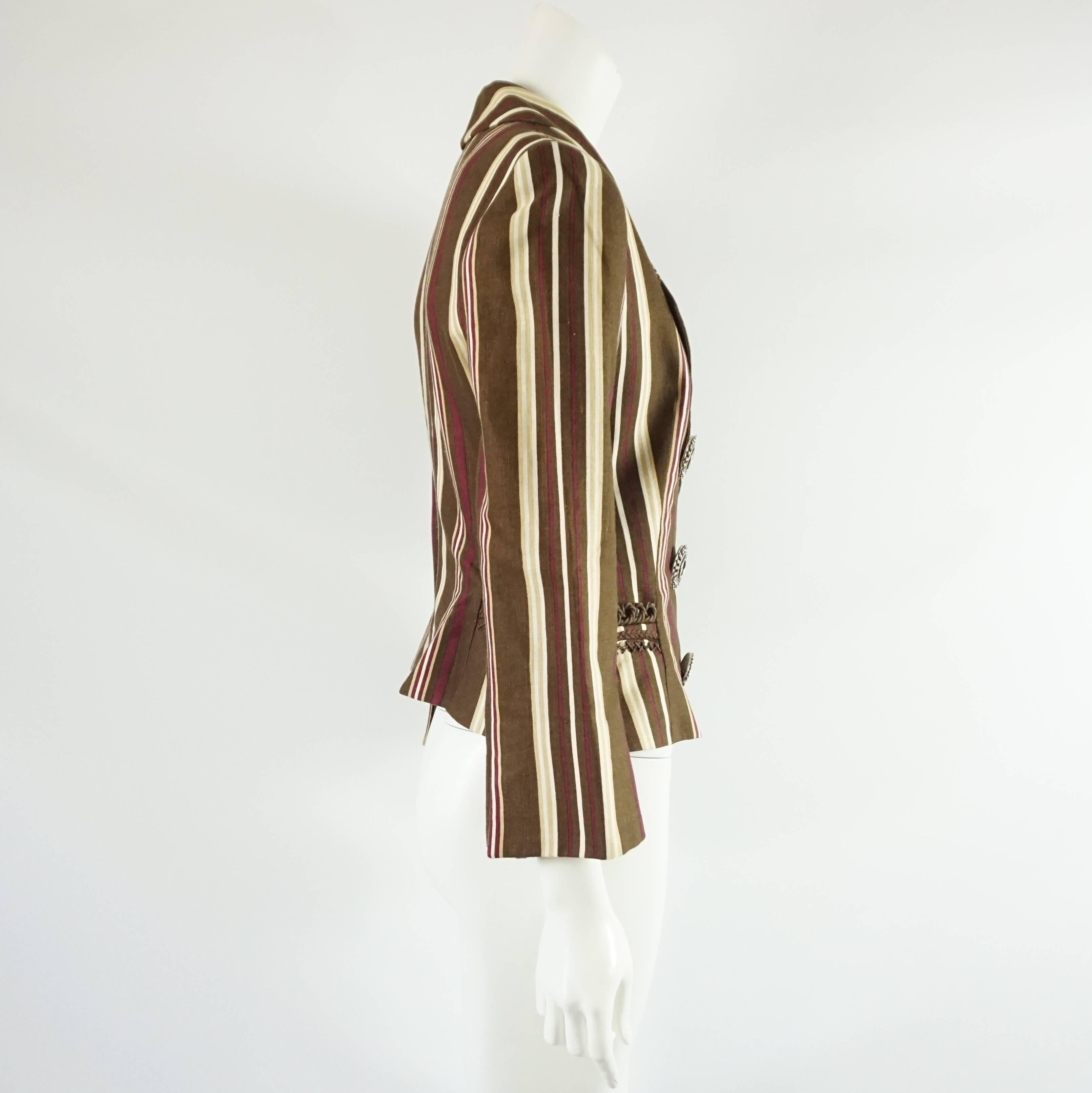 This Christian Dior jacket is made of linen and has a brown, white, beige, and deep magenta striped print. The jacket is single breasted and features two front pockets that have brown rope embroidered detail and large silver etched buttons with