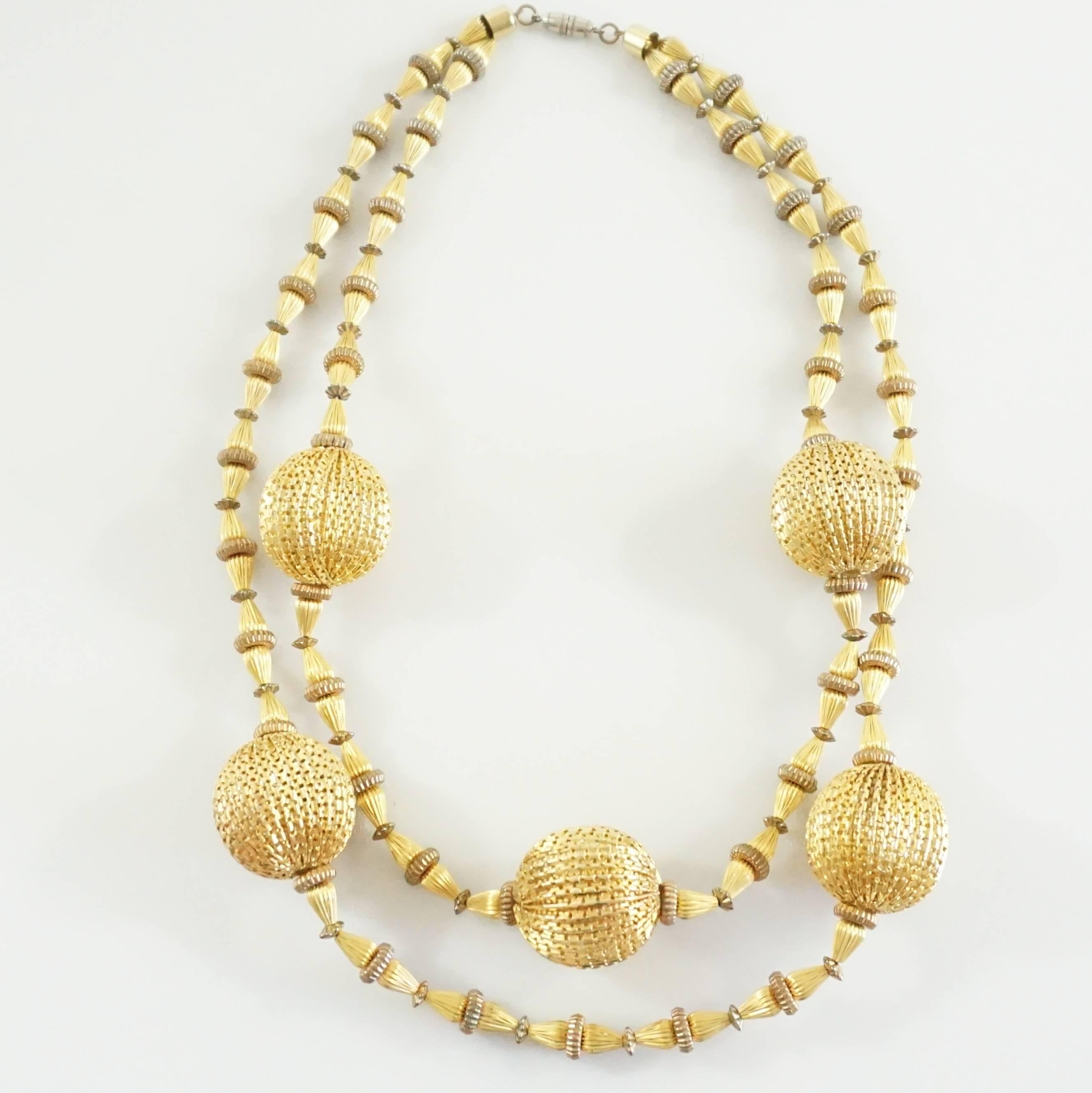 This vintage gold double strand necklace has large etched ball beads with smaller etched beads in between. The clasp screws on and the necklace falls near the bust. The piece is in excellent vintage condition with minimal wear. Circa 1970's.