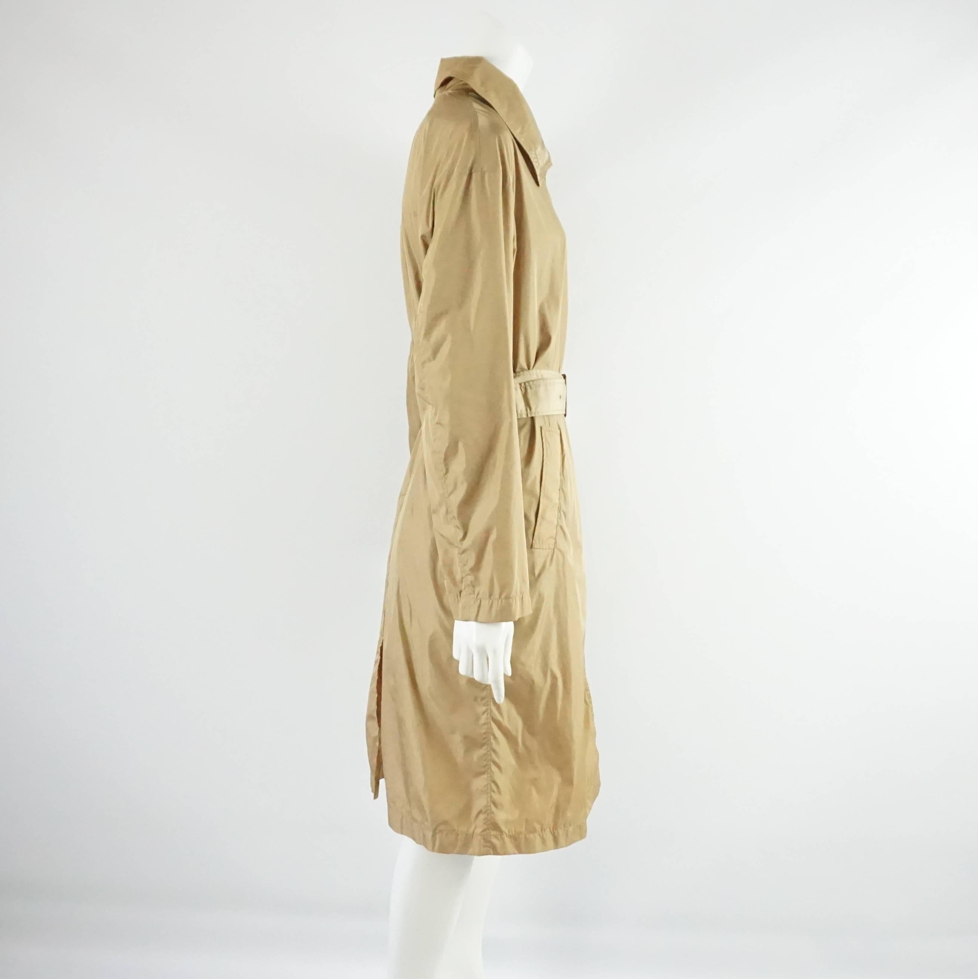 This beautiful Prada nylon trench coat can double as a rain coat. It is tan and features a collar, pockets, and a belt. The back has a slit with a button closure. This coat is in excellent condition with very minor staining. Size