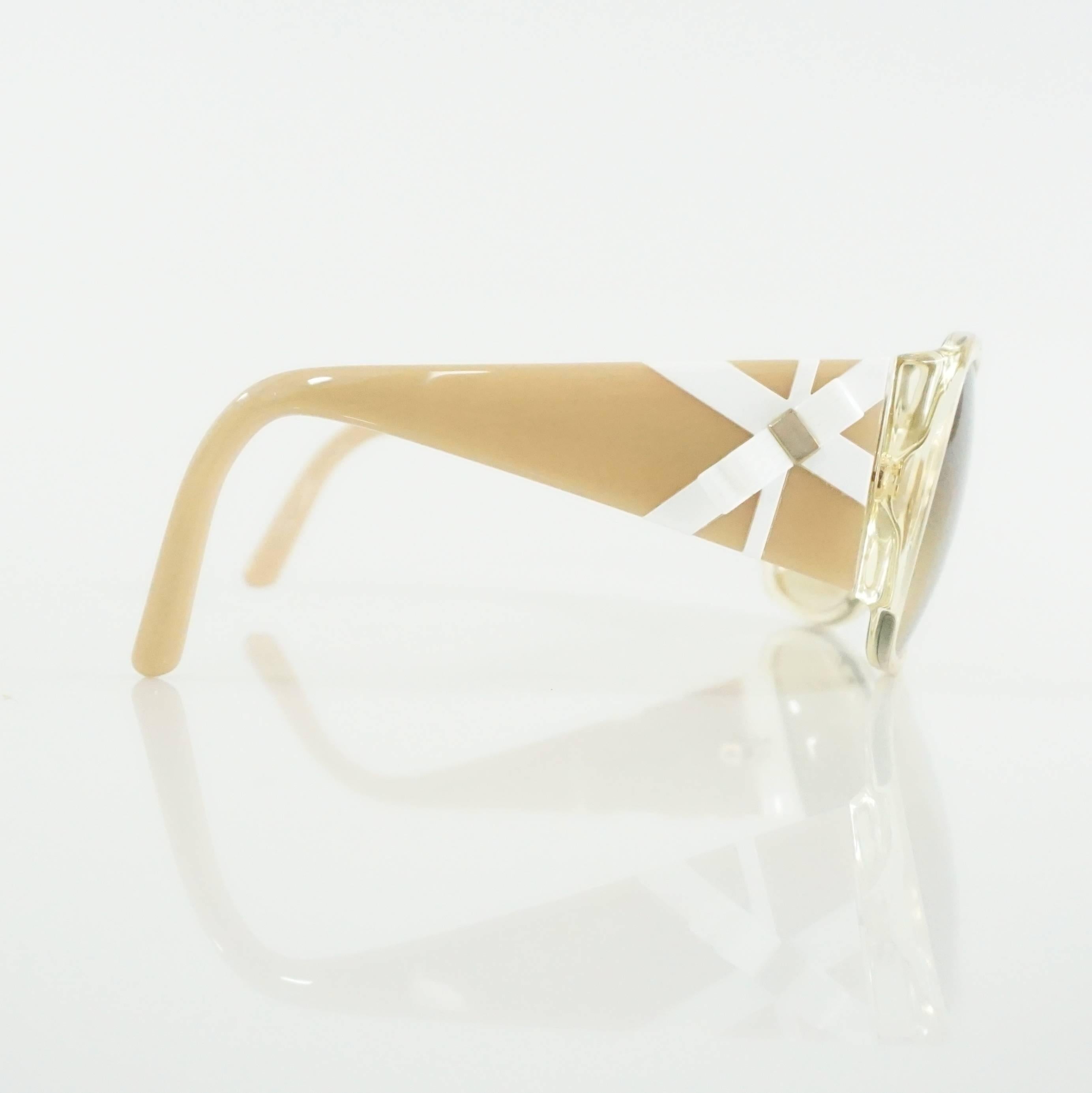 These Versace sunglasses are beige with tan lenses. On the sides are white detailing and a white bow with gold detailing. These sunglasses are in excellent condition.

Measurements
Front Length: 5.5"
Leg Length: 4.75"
Length of Lens:
