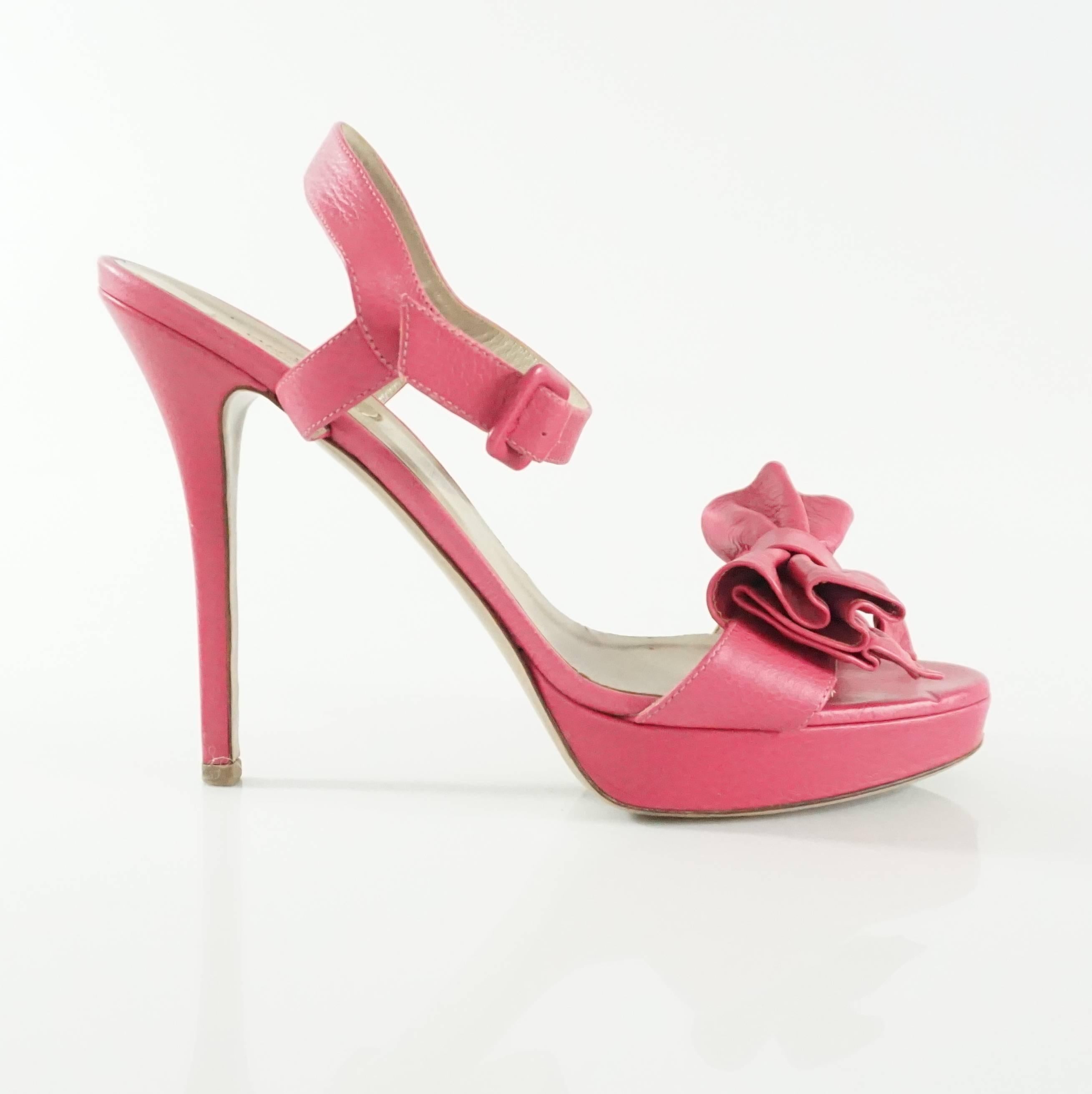 These Valentino pink leather platform heels have a large bow in the front and an ankle strap. They are in good condition with some wear to the leather on the back of the heel, bottom, and platform as seen in the images. Size 41.