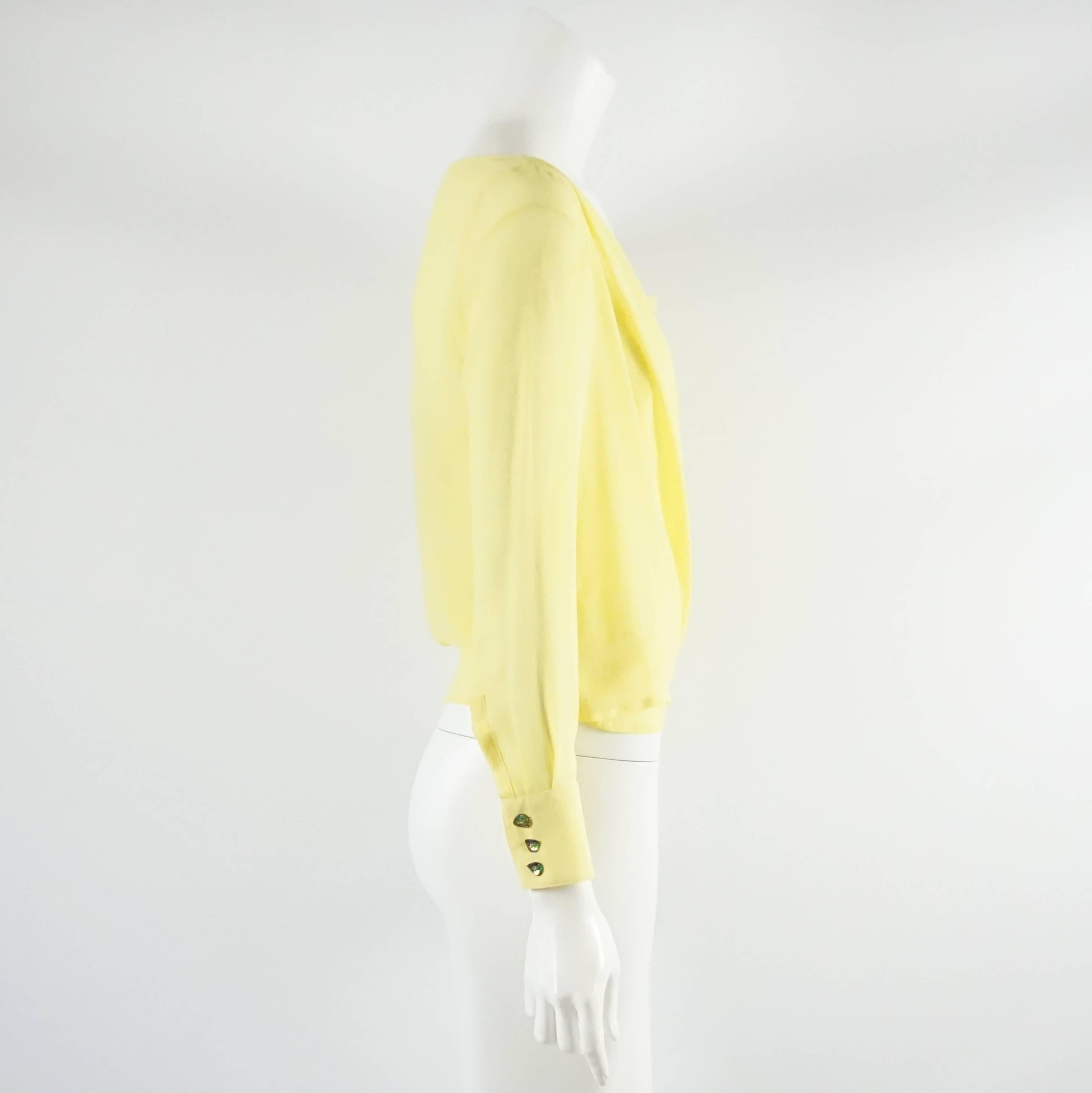 This Versace yellow silk chiffon blouse is a surplice style and comes with a sheer silk tank top that goes underneath. The blouse is long sleeved and has multi color rhinestone cuff buttons. The tank top has small openings in the back with crystal