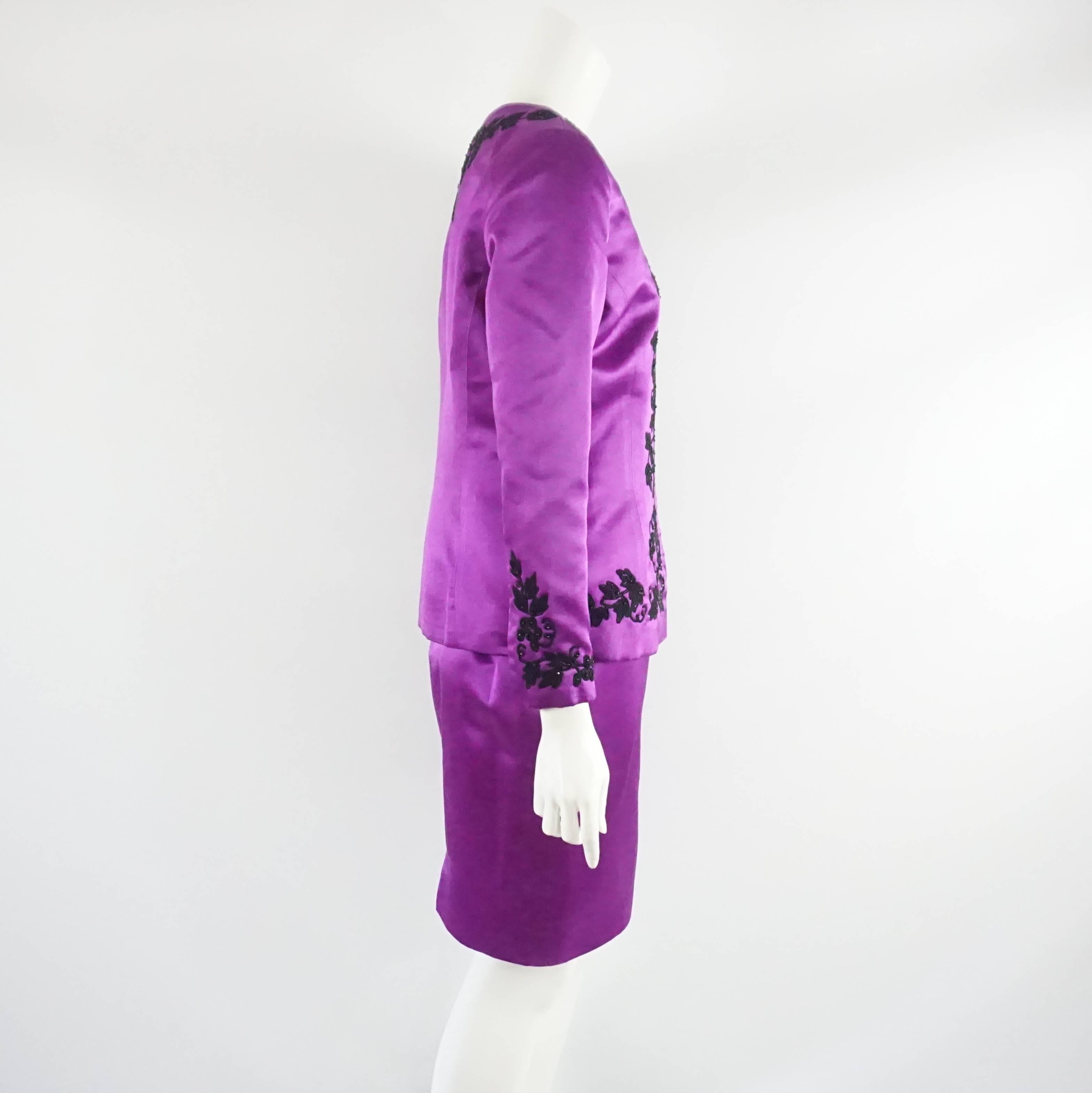 This Oscar de la Renta purple satin skirt suit is a fabulous set. The jacket has a round neck and various clusters of elegantly beaded soutache along the bodice. The skirt has a band at the waist with elastic bands on the sides and a back zipper as