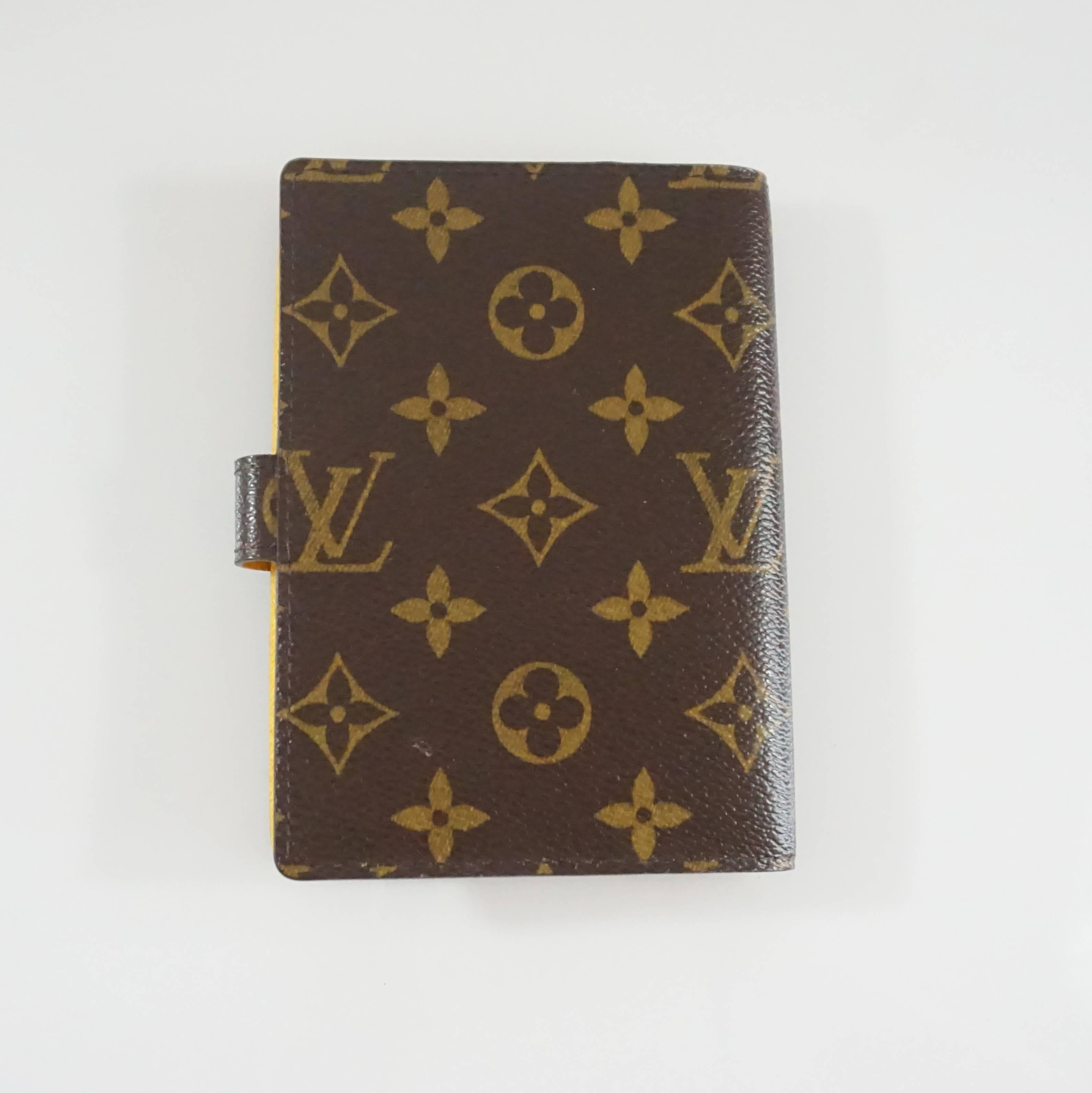 This Louis Vuitton agenda is the classic brown monogram print. The front also features an ivory and a mustard stripe going down the front along with a picture of a bellboy carrying luggage. The inside is the same mustard color with 3 card slots, 2