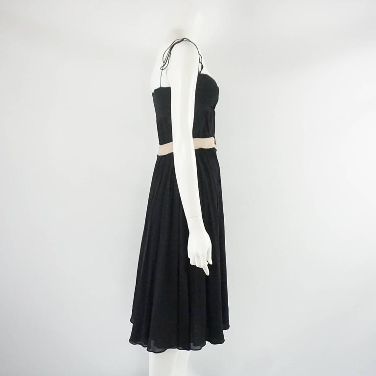 This Alessandro Dell'Acqua black silk dress has spaghetti straps and a loose fit. The bodice criss-crosses and the straps tie at the tops. The dress also has a beige pseudo-belt with rhinestones and sequins. The piece is in good condition with some