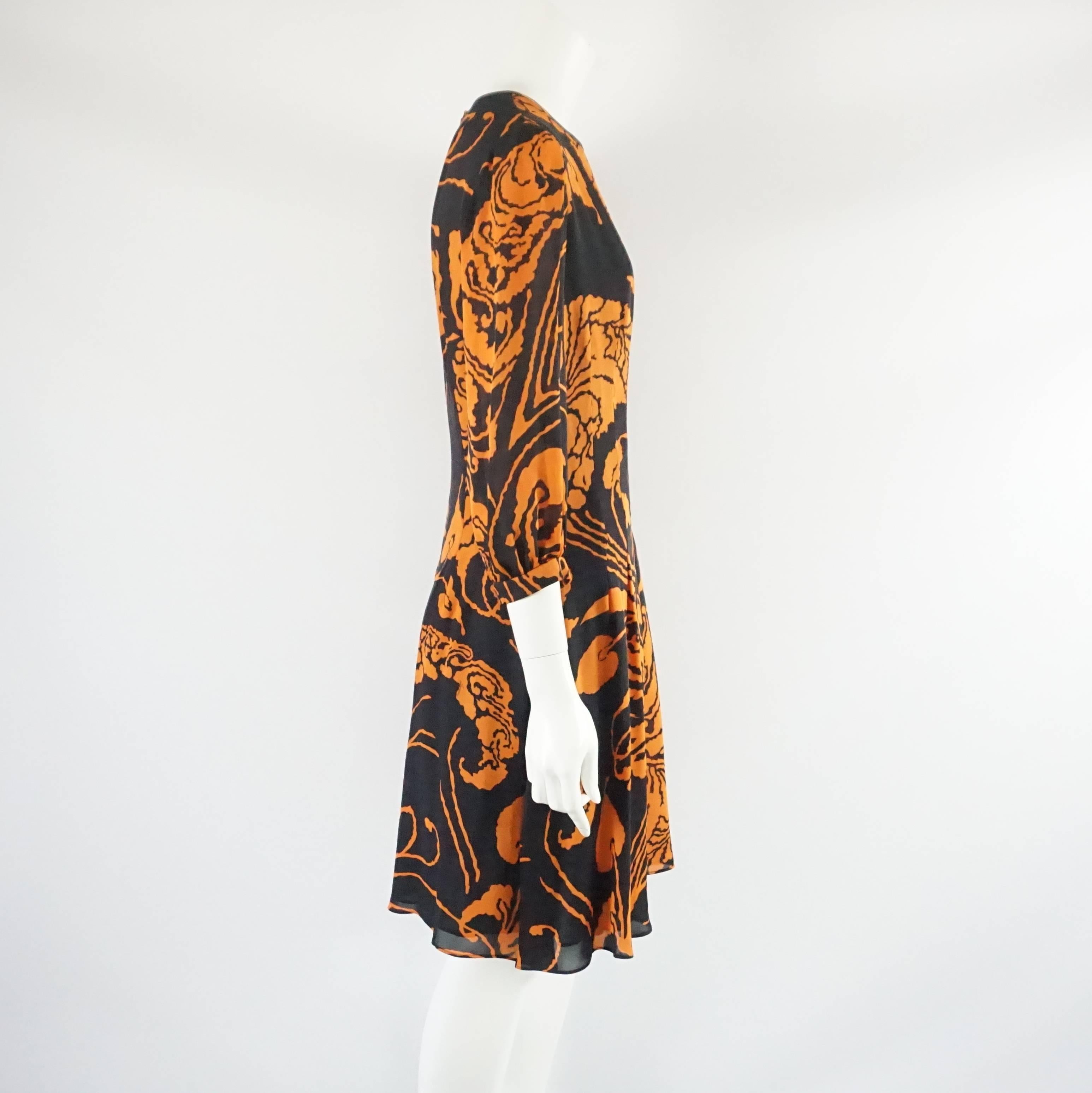 This Gucci dress has a beautiful orange and black abstract print on it. The dress has a round neck with 3/4 puffed sleeves and Gucci emblem cuff buttons. It also has pleated along the skirt and a back zipper. The piece is in excellent condition with