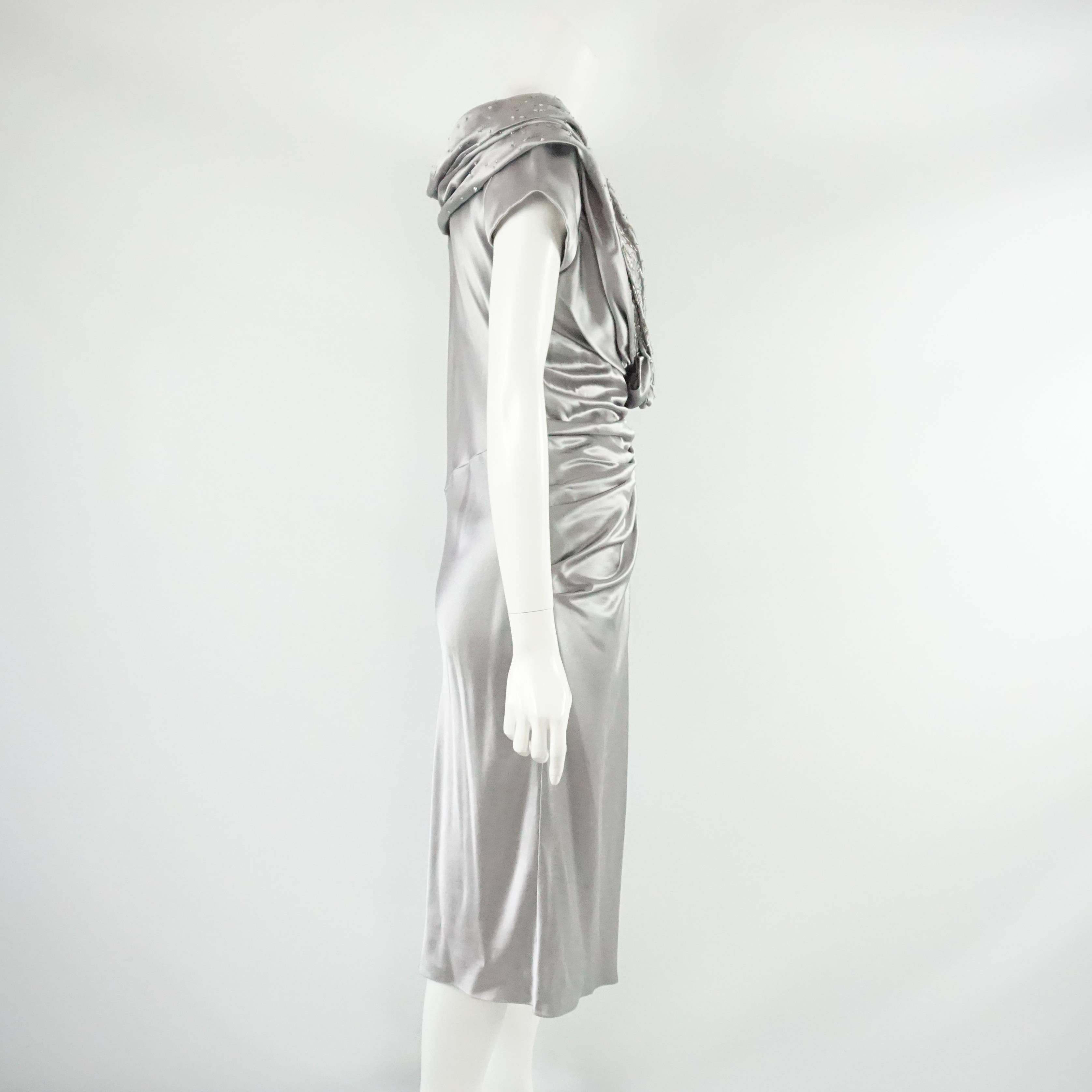 This Christian Dior silver satin dress has ruching all along the front and a plunging neckline. The neckline also has a rushed flower at the bottom and small silver beads all along the bodice. The dress is in good condition with some pulls and beads