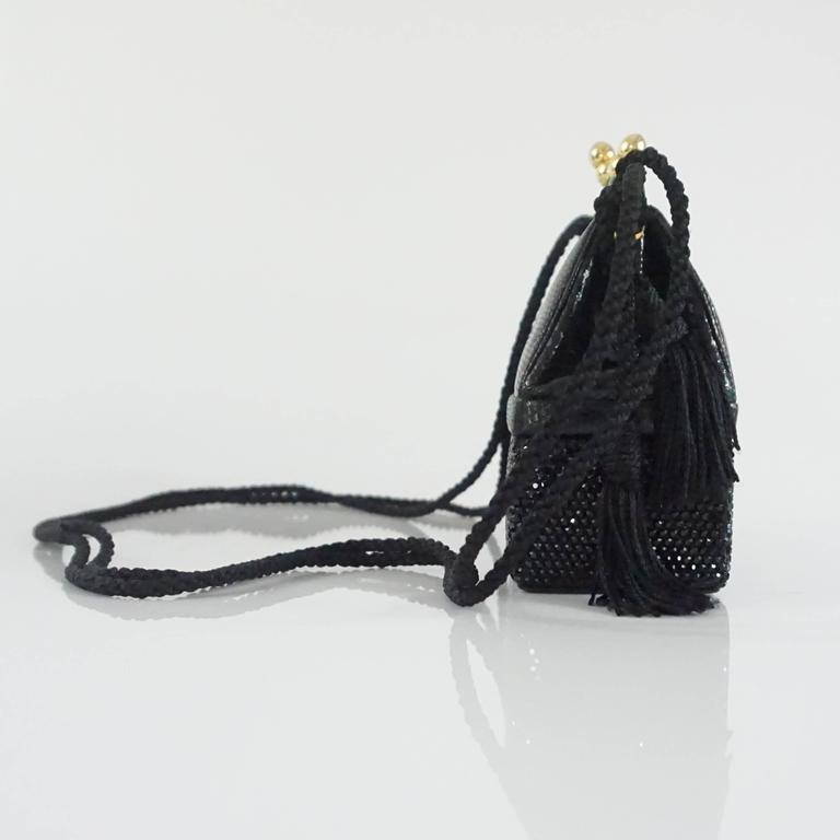 This Judith Leiber black evening back is structured with a top frame and snap clasp. The bag is made of lizard and black rhinestones and also has a bottom compartment as seen in the images. The evening bag has a rope cross body strap with hanging