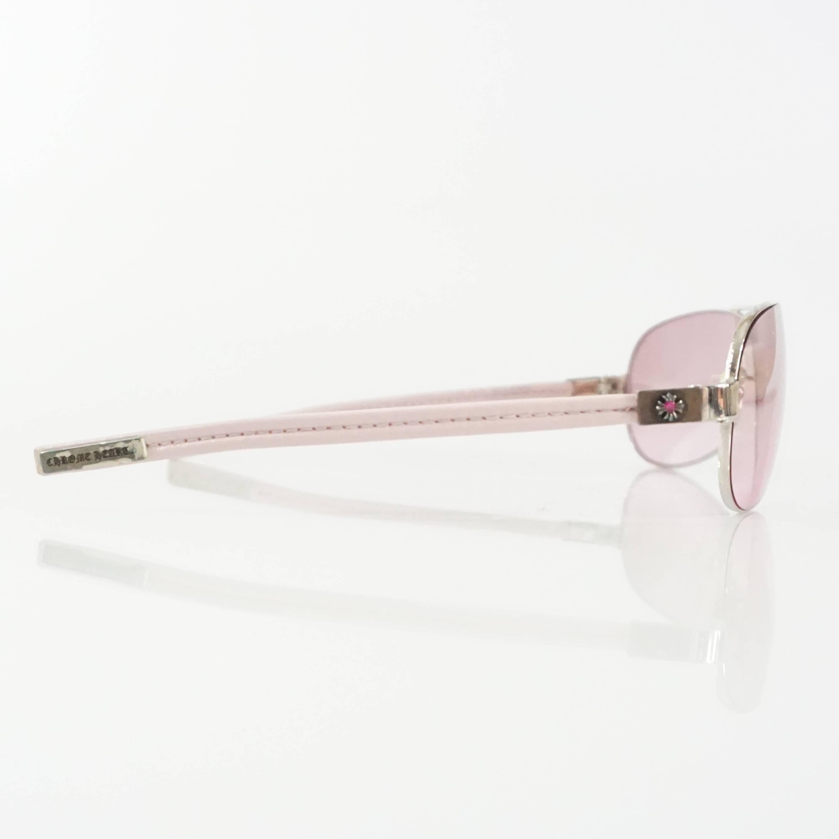 These Chrome Hearts sunglasses feature pink lenses and legs covered in pink fabric. They have a pink rhinestone and silver detailing on the side close to the lenses. These sunglasses are in very good condition with very minimal